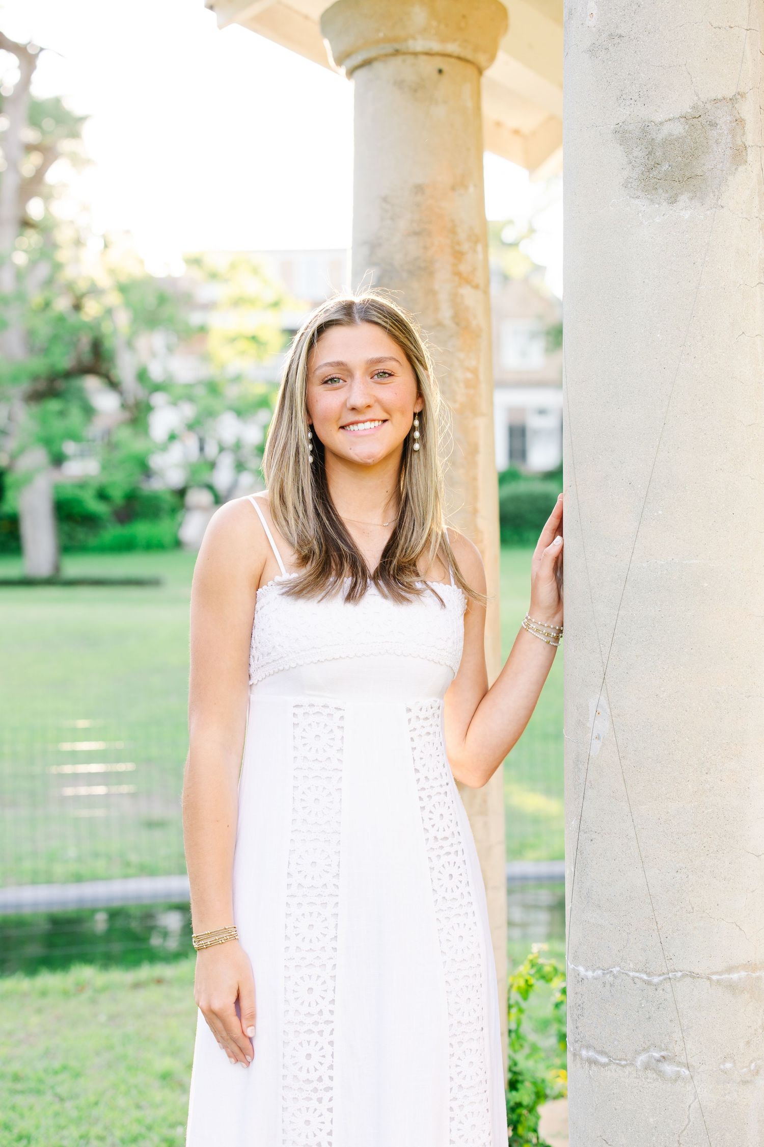 Elegant white dress portrait under a stone gazebo with garden backdrop.