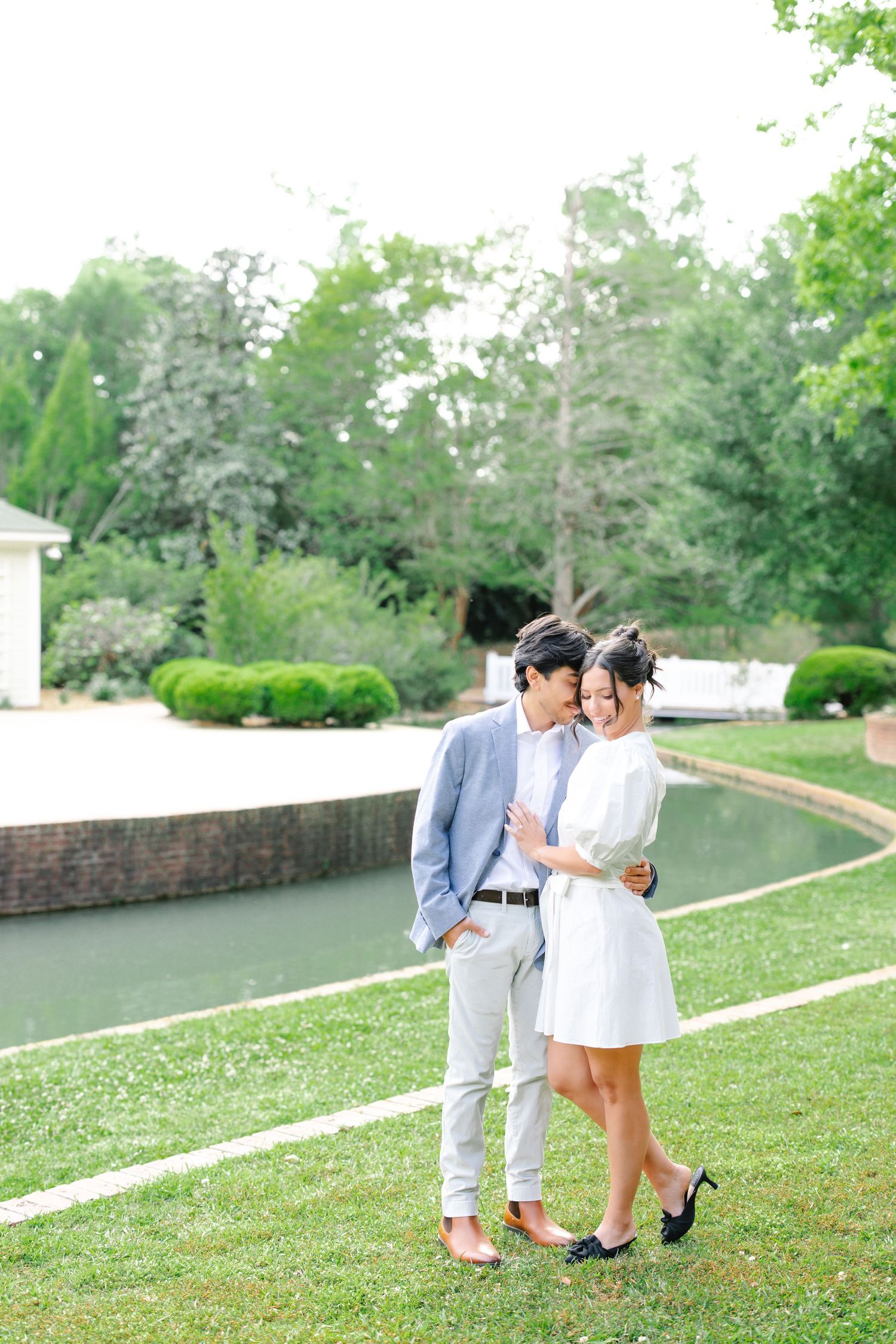 Couple in coordinated white and blue outfits share an intimate moment in a manicured garden setting.