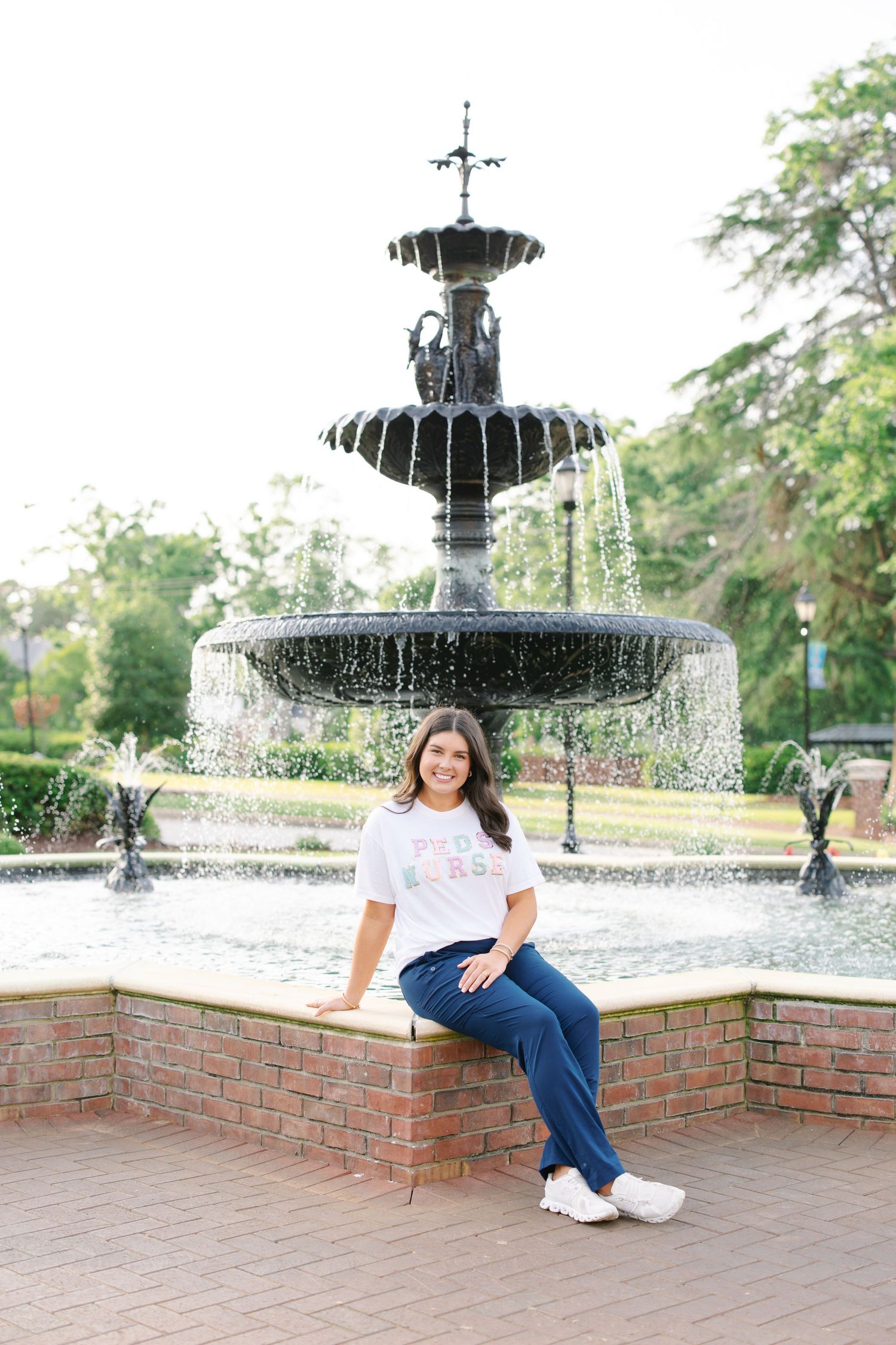 Graduate relaxes by ornate tiered fountain wearing casual attire at university.