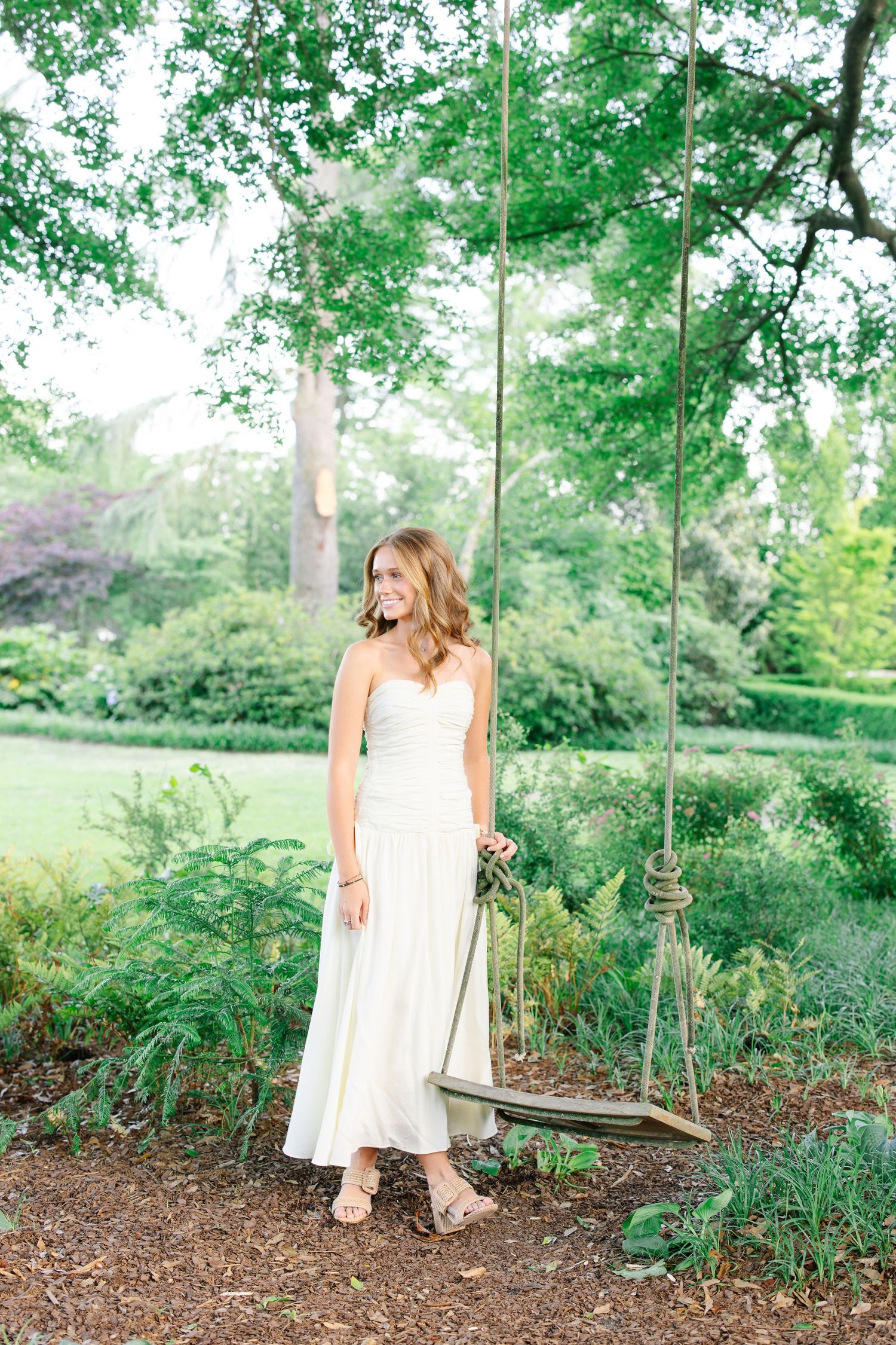 Garden scene featuring a white dress and wooden swing surrounded by lush greenery.