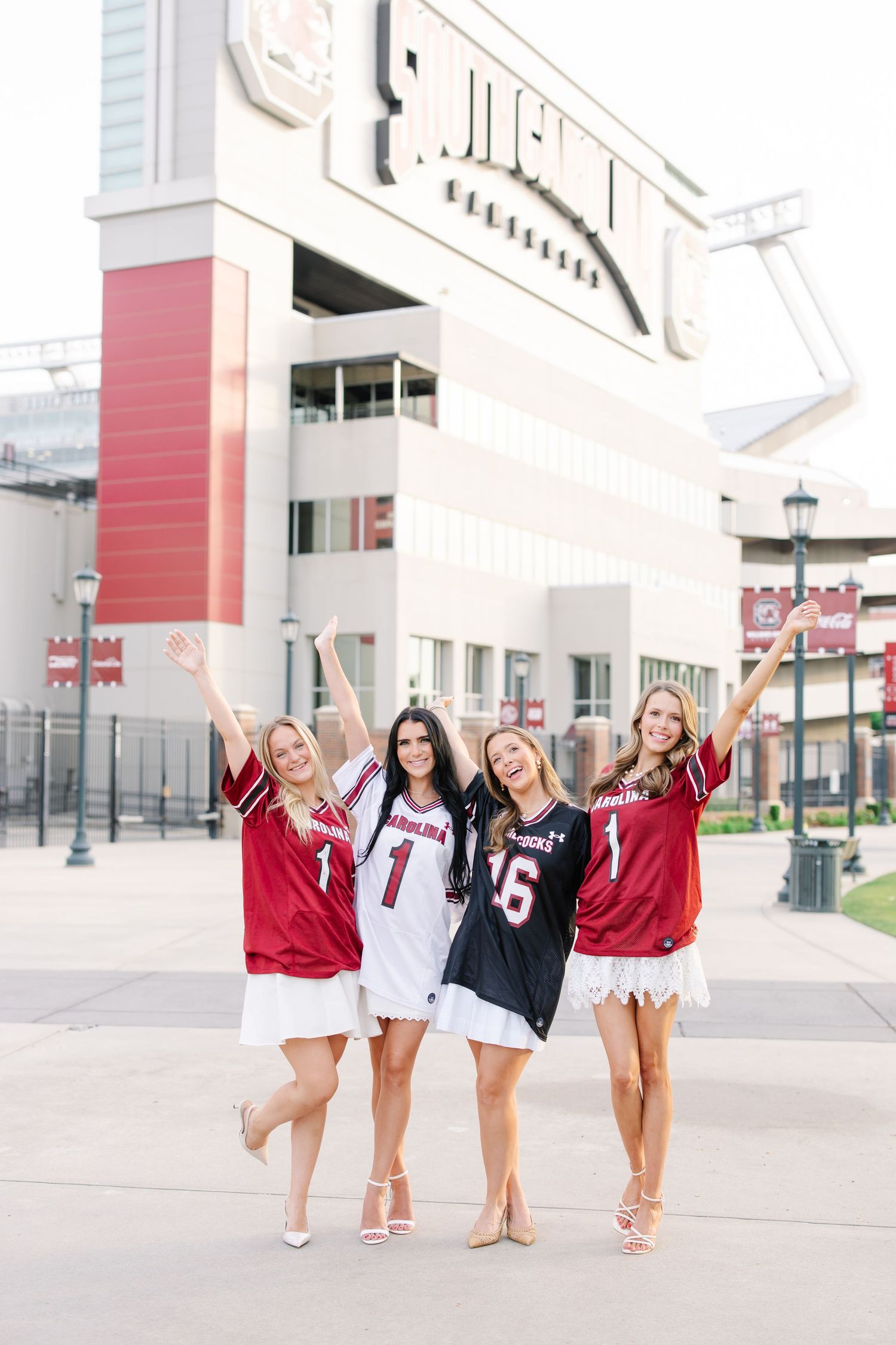 Four friends in sports jerseys pose excitedly outside a stadium building.