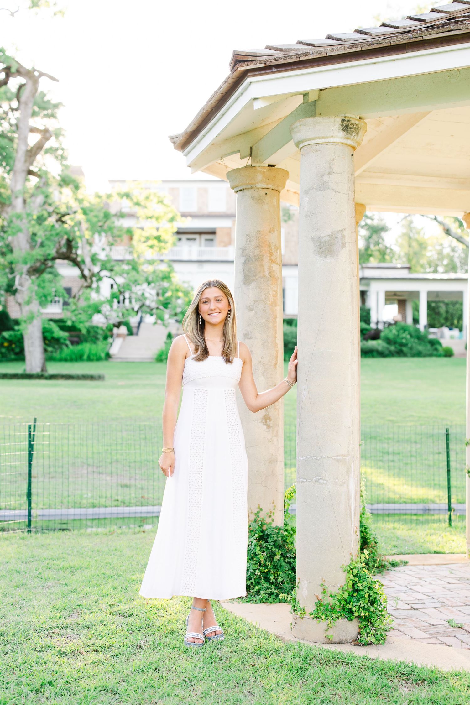 Full-length portrait in white dress standing between classical stone columns.