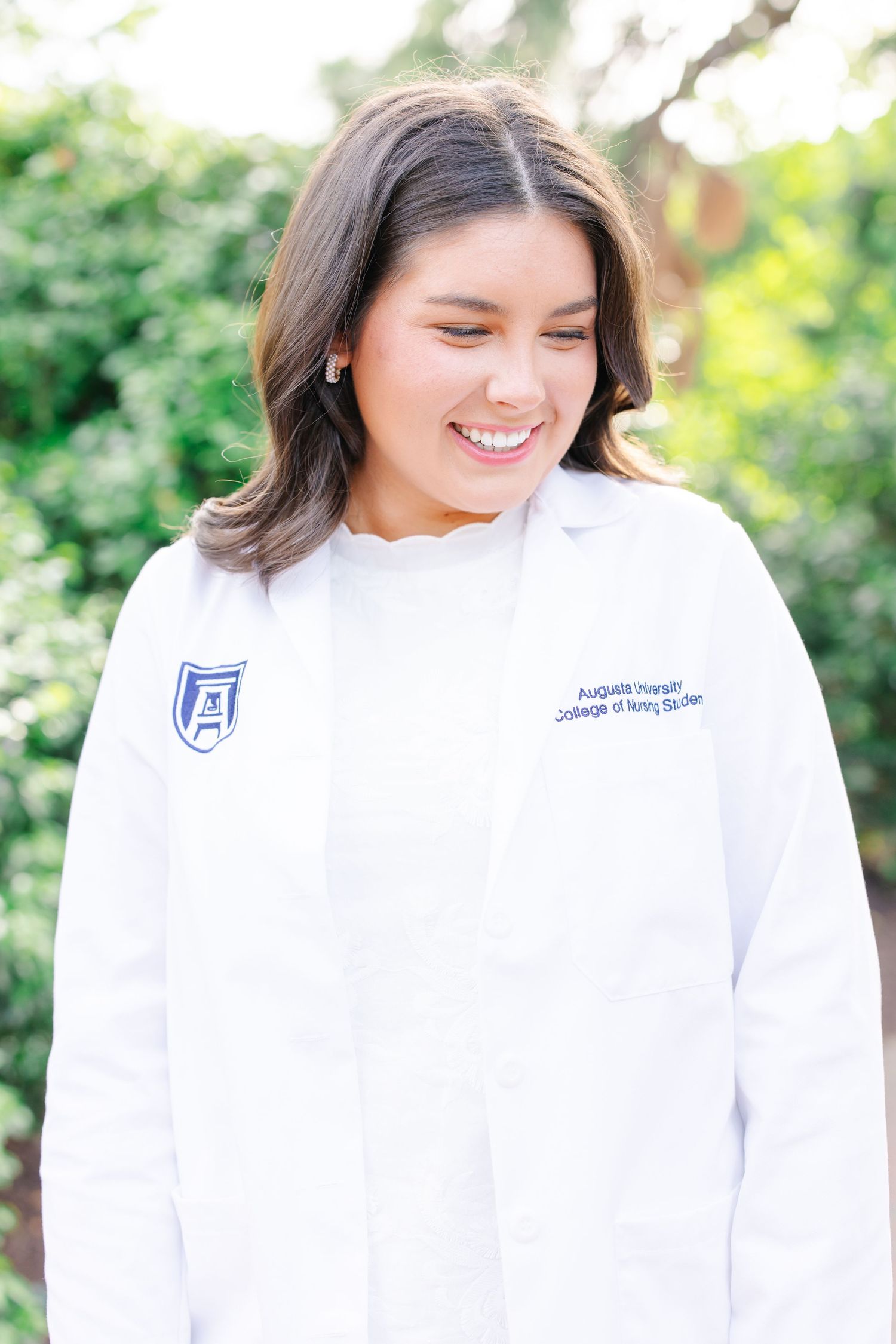 Medical student in white coat smiles during professional headshot on campus.