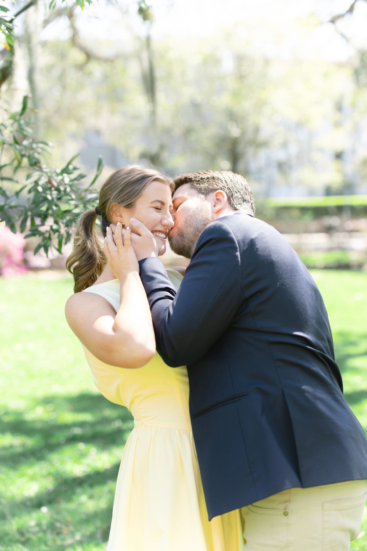 A romantic outdoor engagement photo with a couple in yellow dress and navy blazer.