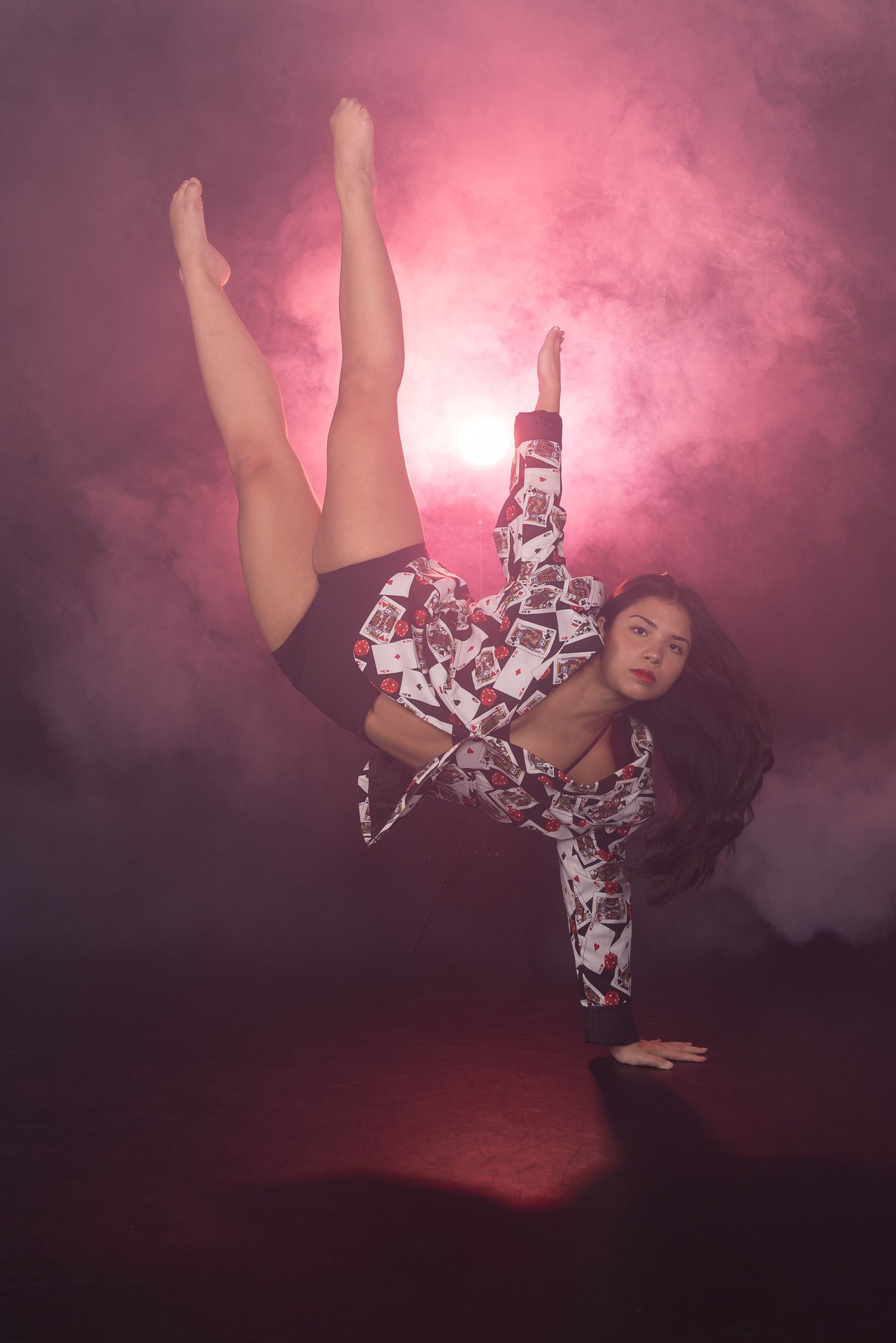 Dancer performs expressive movements in patterned outfit against pink smoky backdrop.