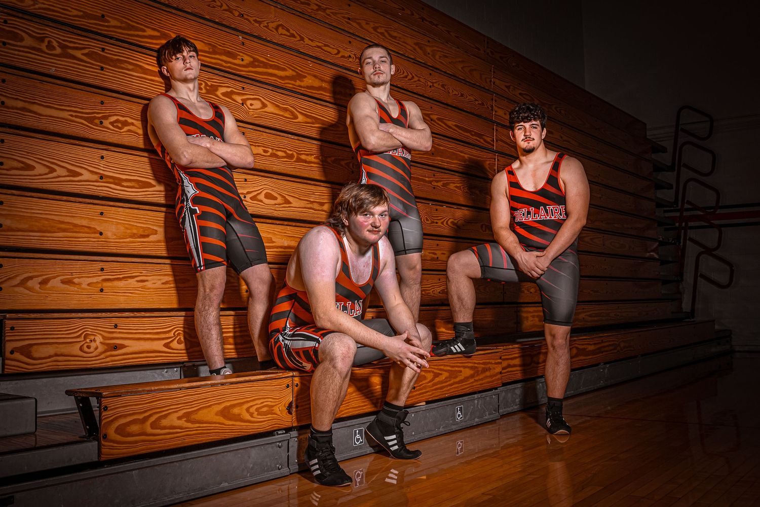 Athletes sit on wooden bleachers in dramatic lighting for sports team photo.