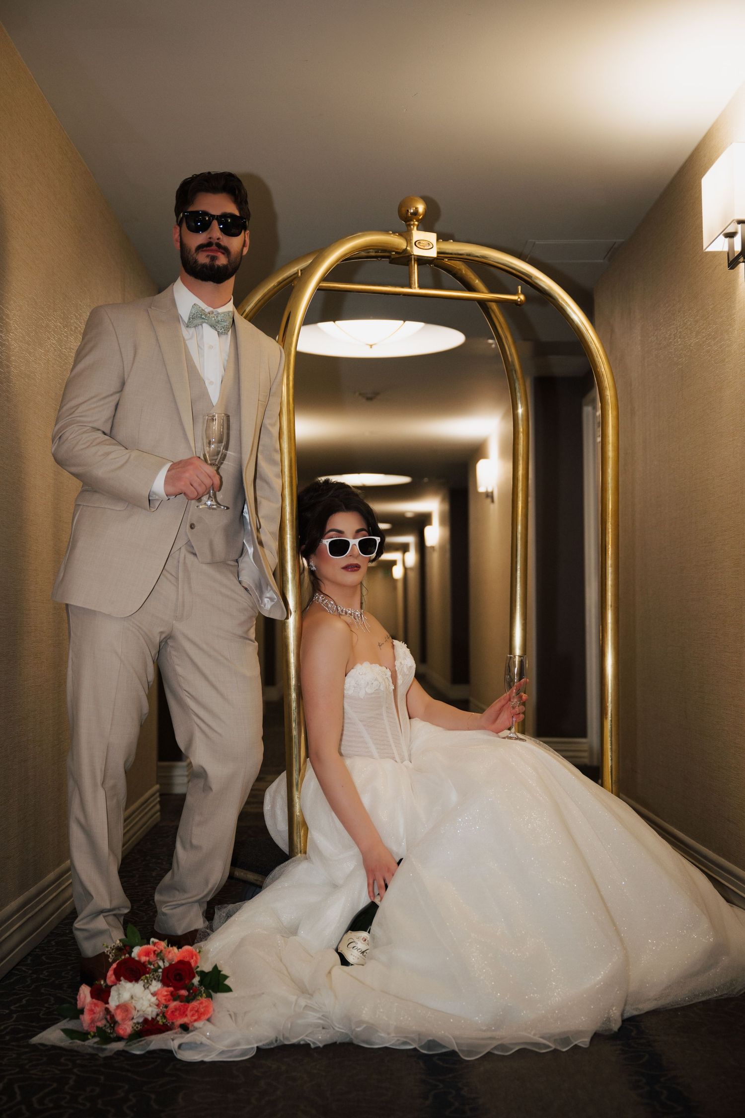 Boise, Idaho Wedding Couple at The Grove Hotel. A couple poses dramatically in a hotel hallway with a gold luggage cart and flower bouquet.