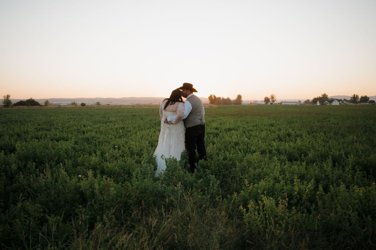A couple walks together through a lush green field during sunset creating a romantic silhouette against the horizon.