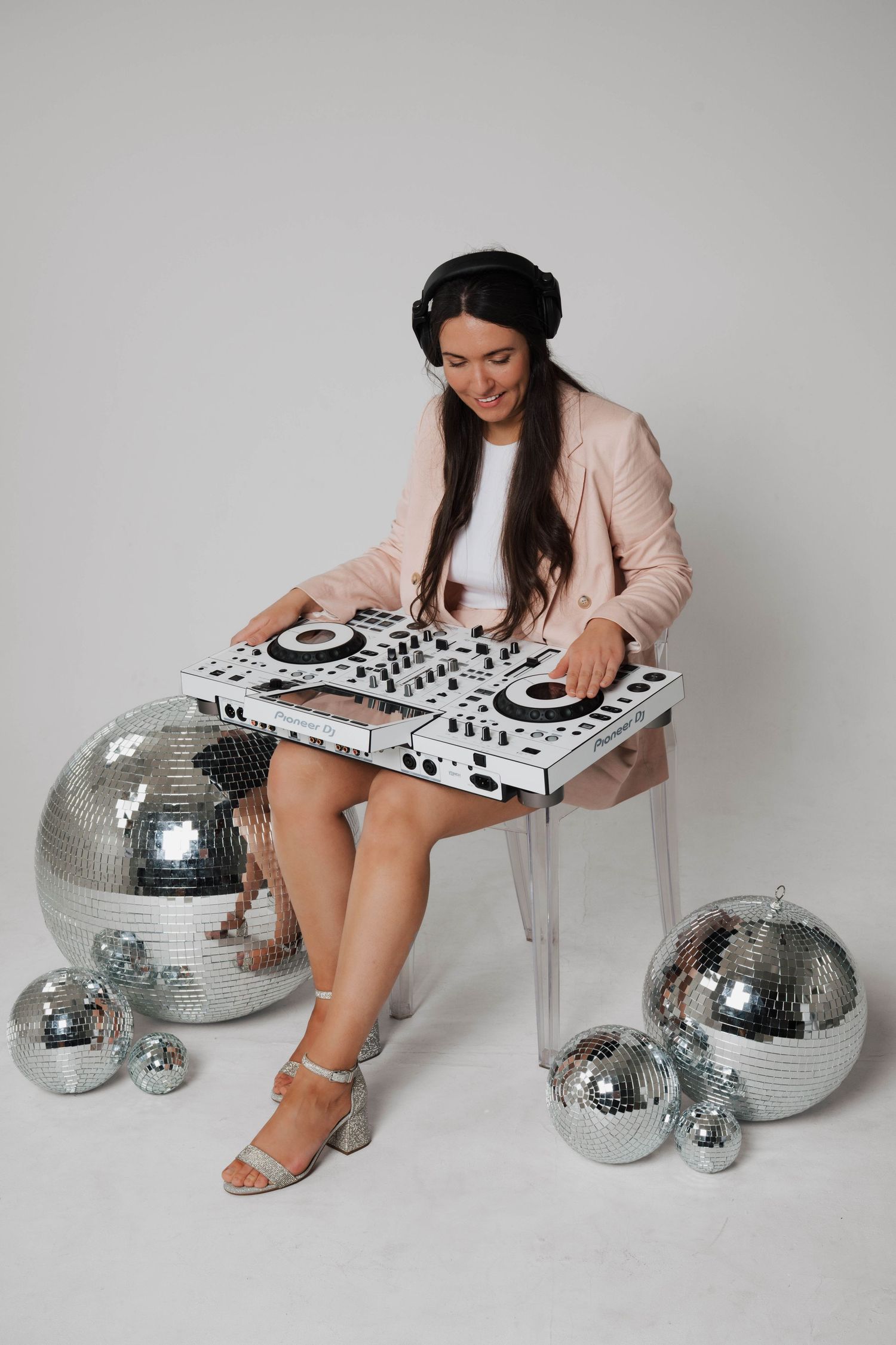 A modern DJ setup with silver disco balls arranged against a white backdrop with someone performing in a pink sweater.