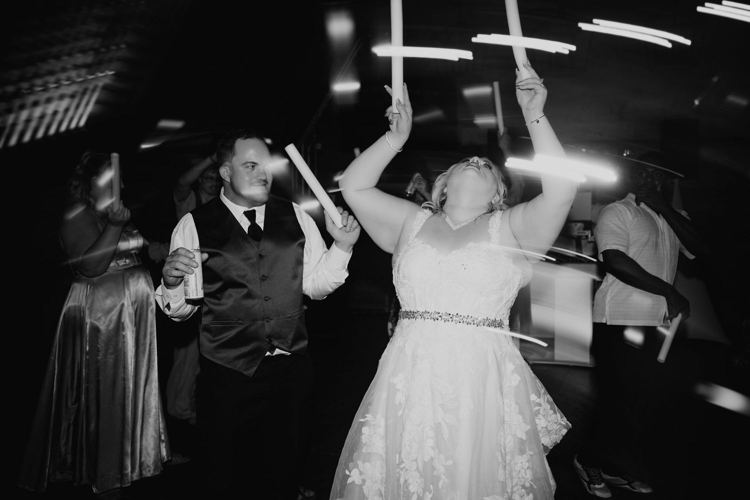 Wedding party attendees dance and celebrate together in a black and white photo.