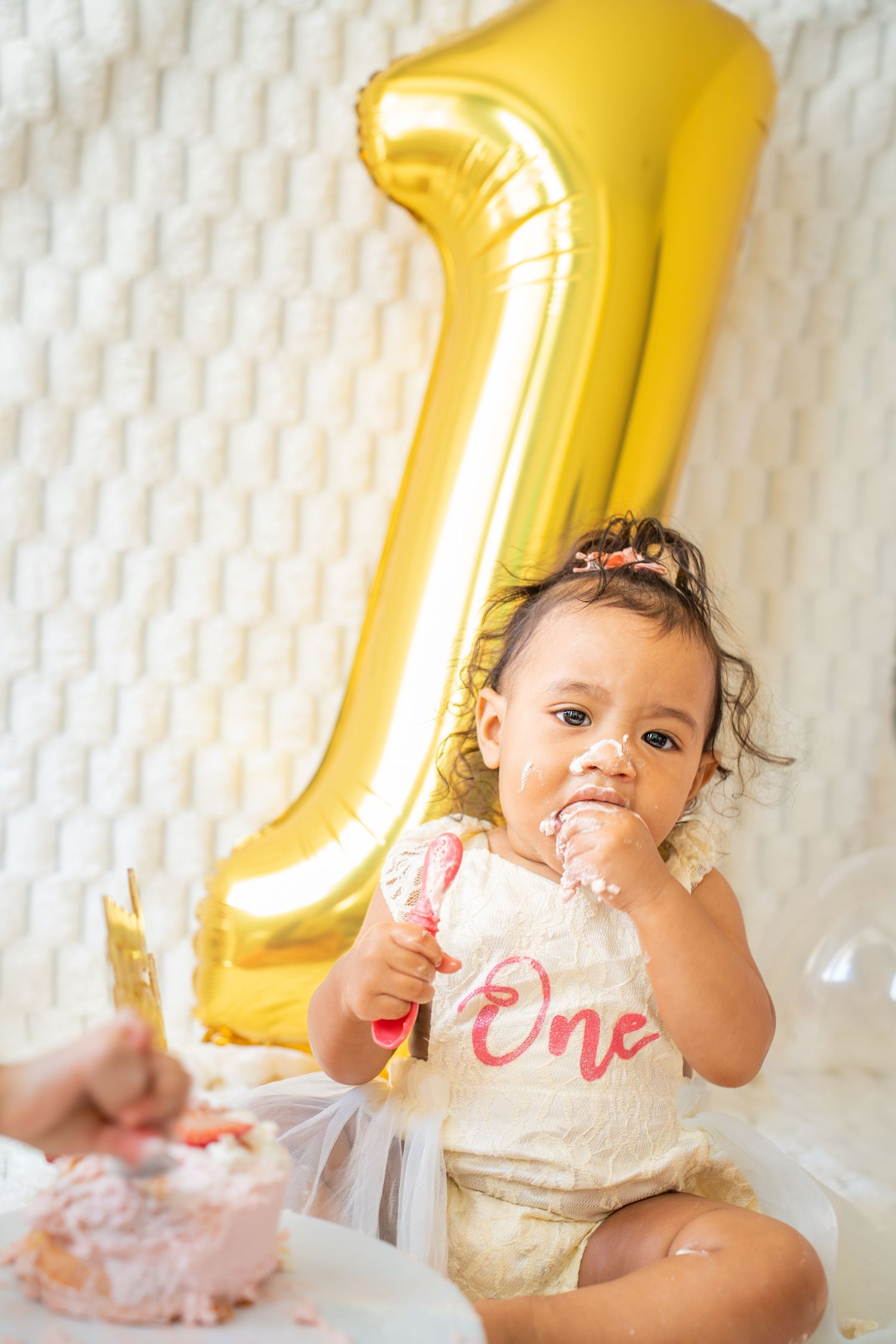 First birthday celebration setup with large gold number one balloon and white textured backdrop.
