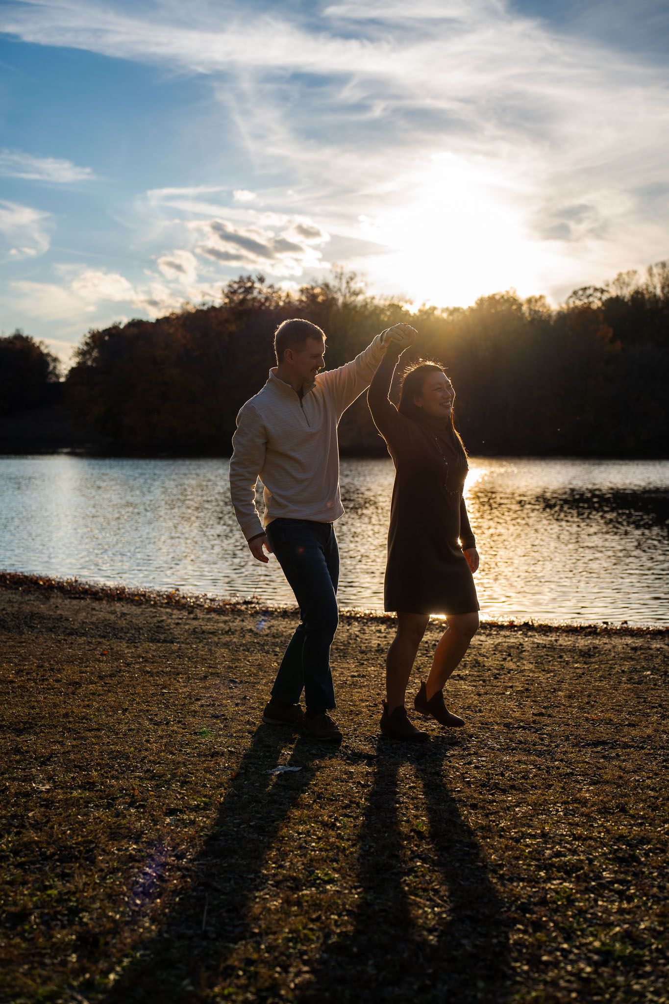 Silhouettes of couple walking along shoreline at dusk with dramatic sunset reflections on water.