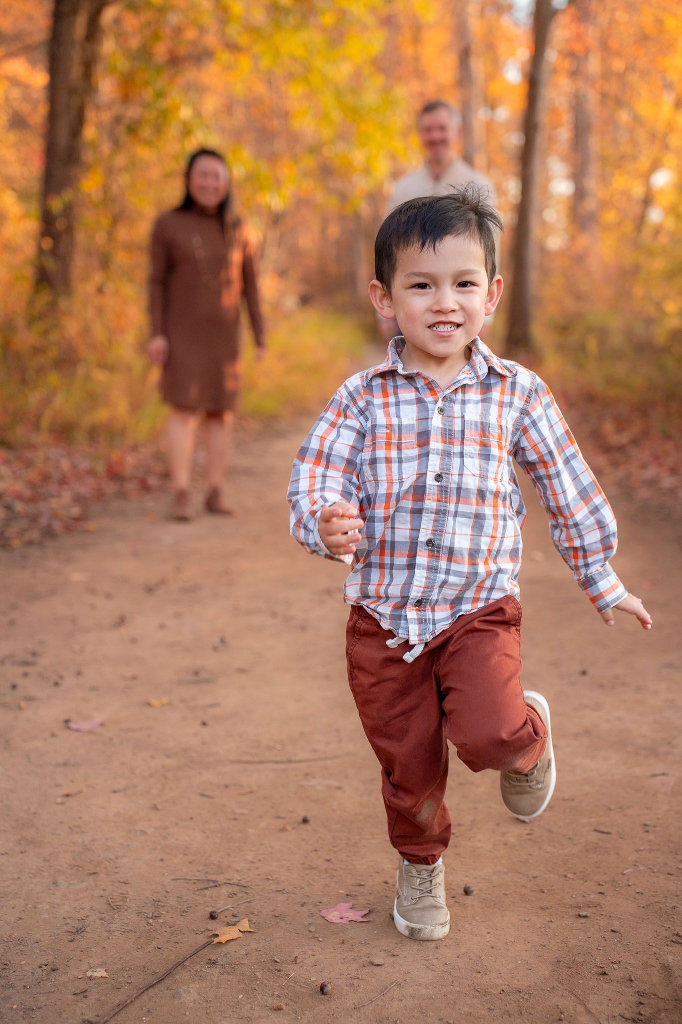 Child running and playing on dirt path surrounded by vibrant fall foliage.
