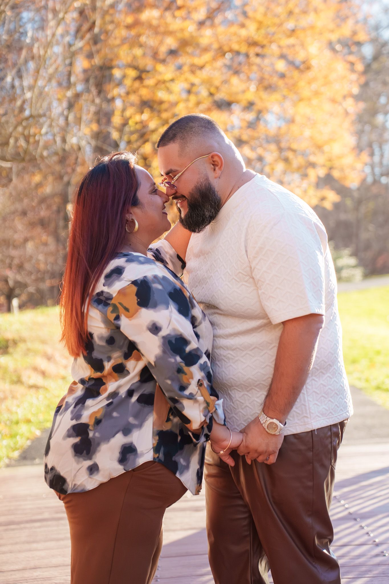 A couple shares tender moments in a park during autumn with golden sunlight filtering through the trees in the background.