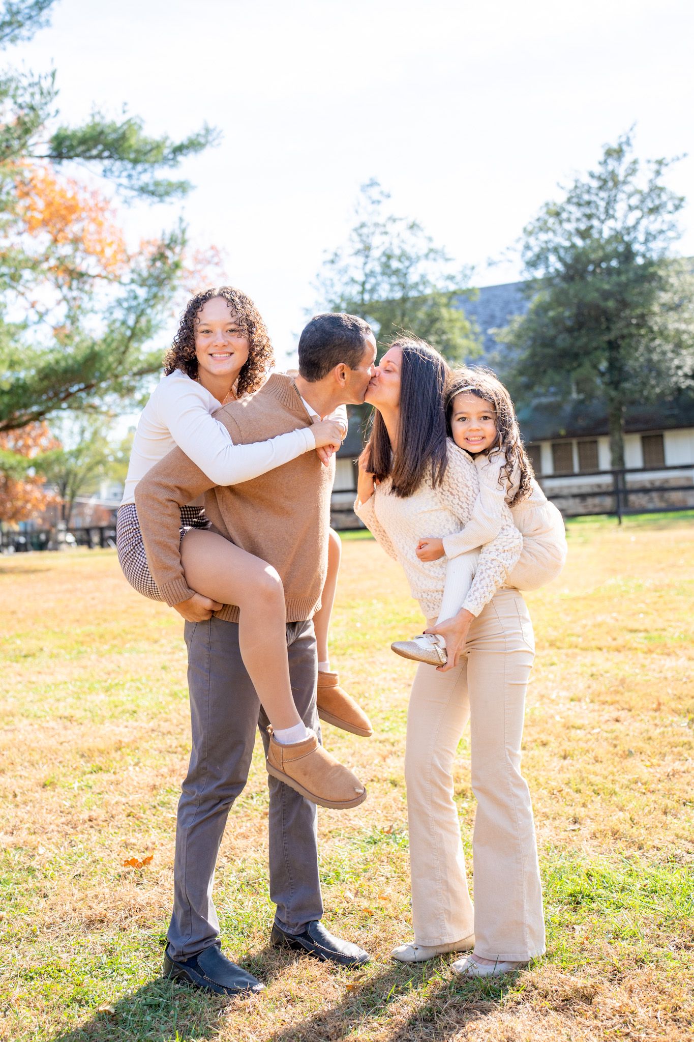A family shares playful moments together in a sunny autumn field wearing coordinated beige and white outfits.