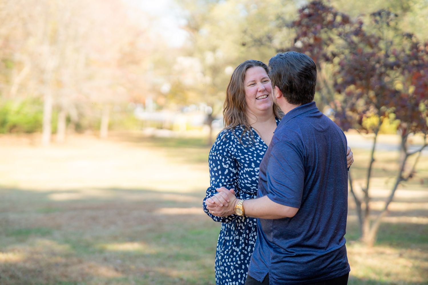 A romantic couple shares an intimate moment while dancing together in a sunlit park setting.