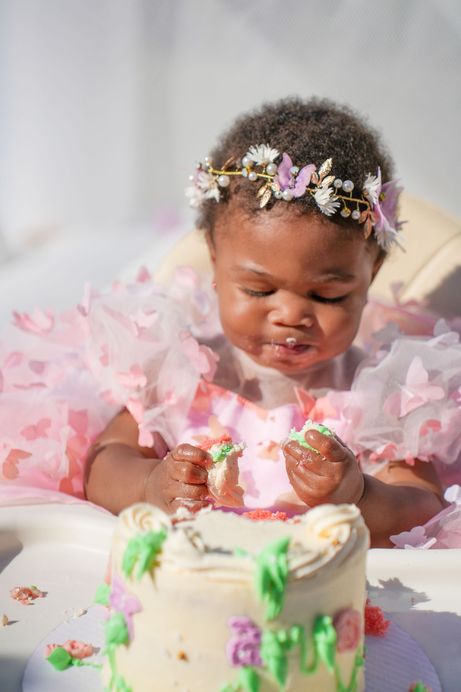 Baby in pink tutu dress smiling and playing with birthday cake during first birthday cake smash photoshoot.