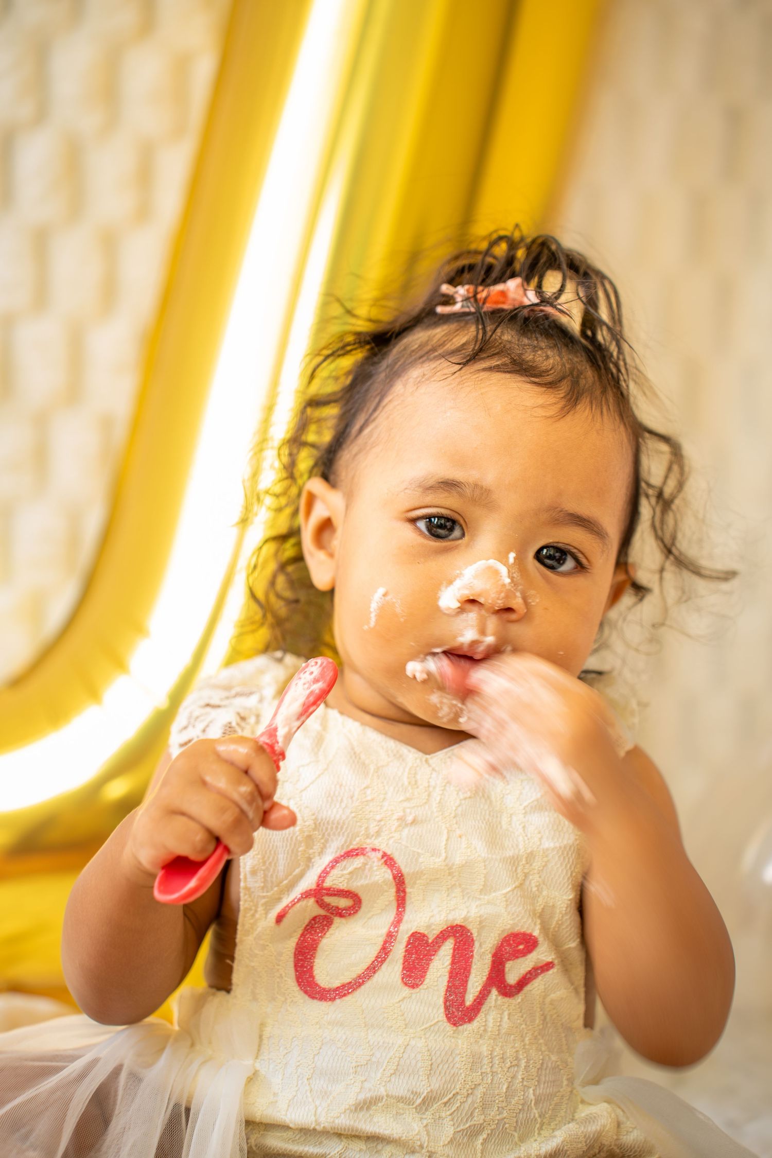 Close-up shots of baby tasting birthday cake during smash cake photoshoot with gold decorations.