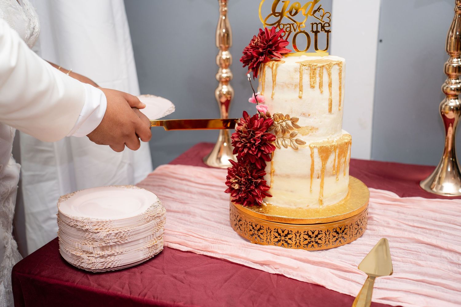 Elegant wedding cake display with gold accents and burgundy floral decorations.