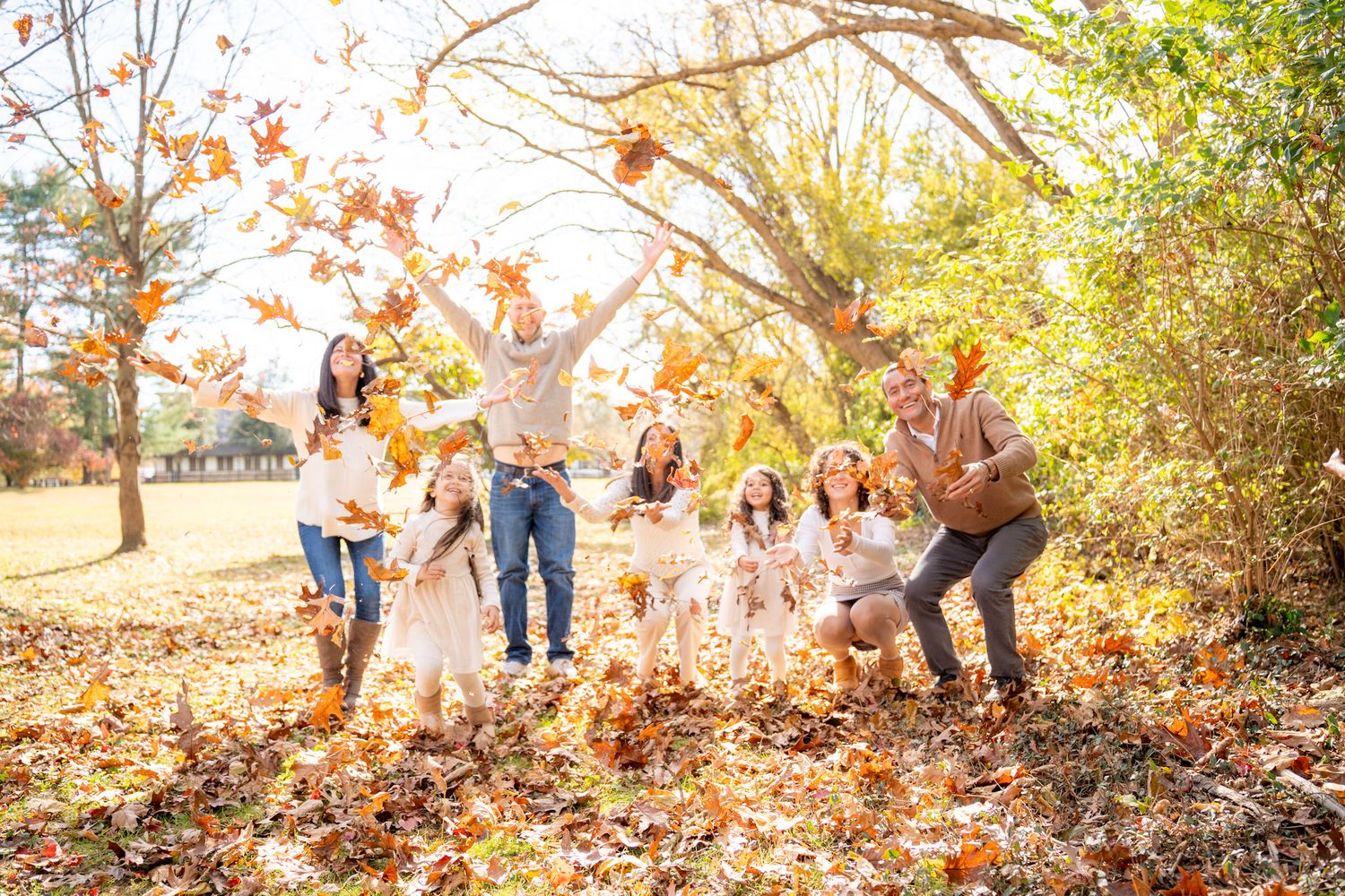 Family enjoying a playful autumn day together in a park with falling leaves during golden hour.