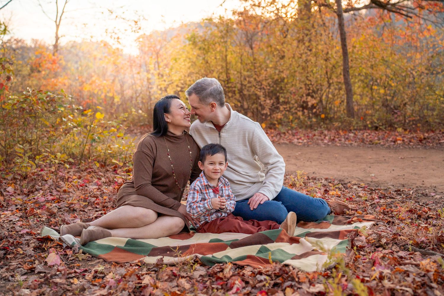 Couple sitting on blanket surrounded by fallen autumn leaves during golden hour sunset in the park.