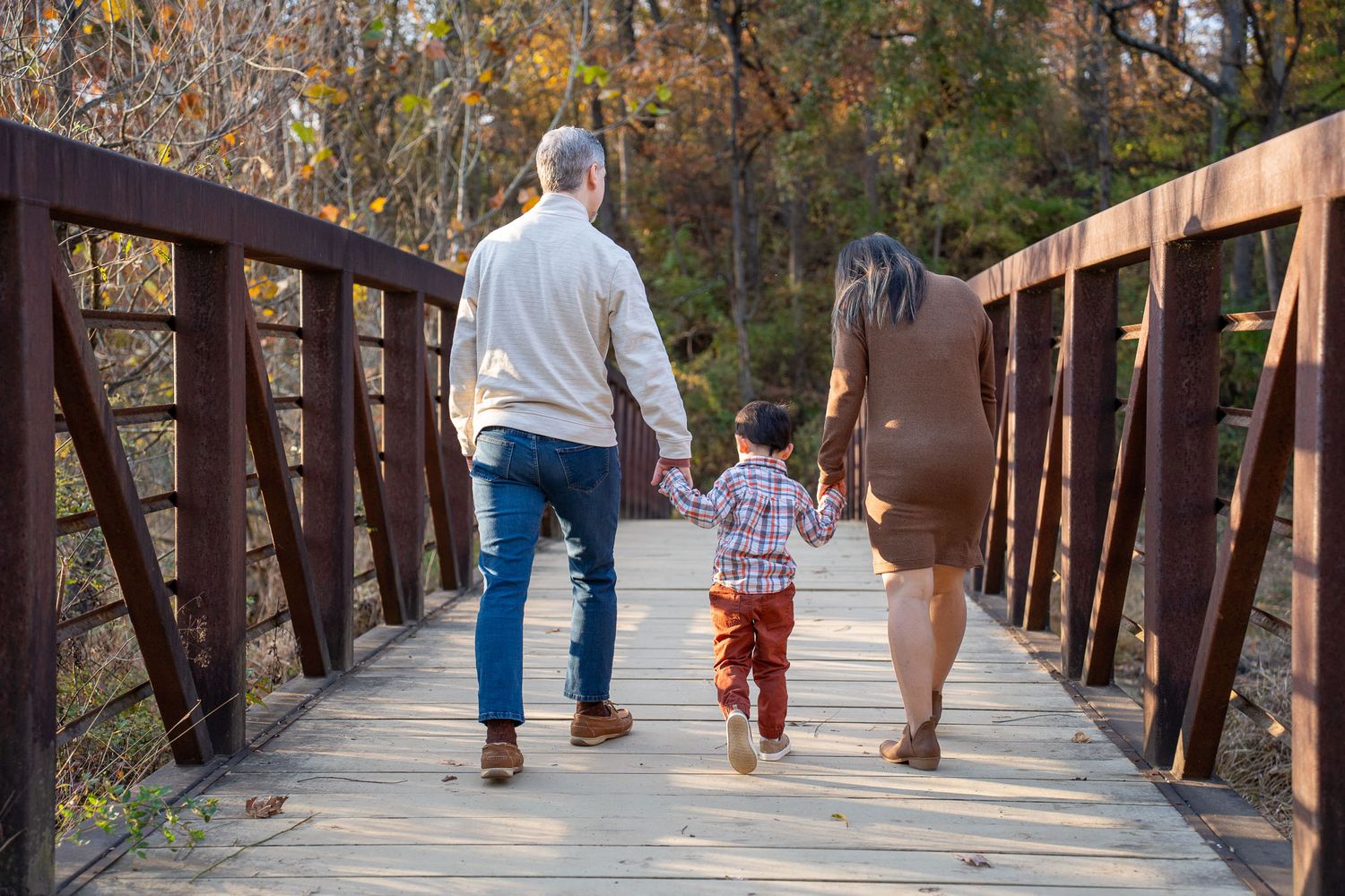 People walking on a wooden boardwalk trail through autumn trees with colorful fall foliage.