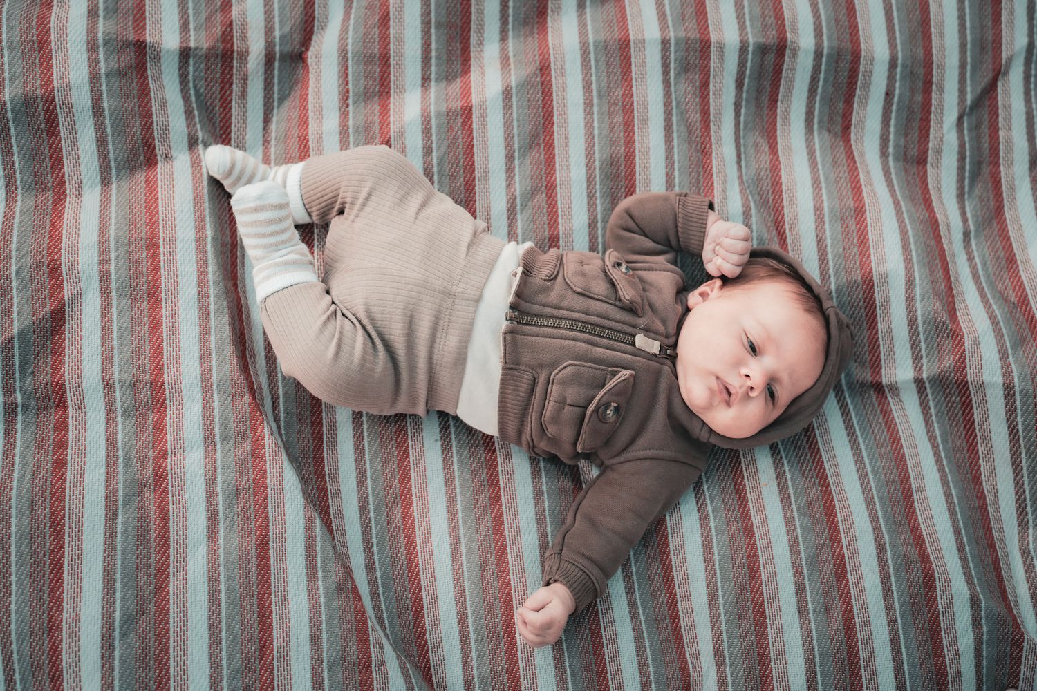 A baby lies on a brown and white striped blanket in multiple poses showing different sleeping positions.