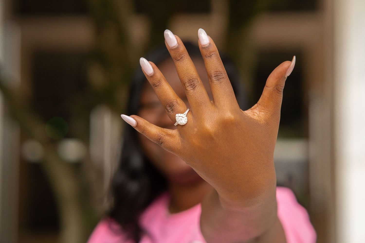 Hands raised in the air show off sparkling engagement rings and wedding bands against a blurred background.