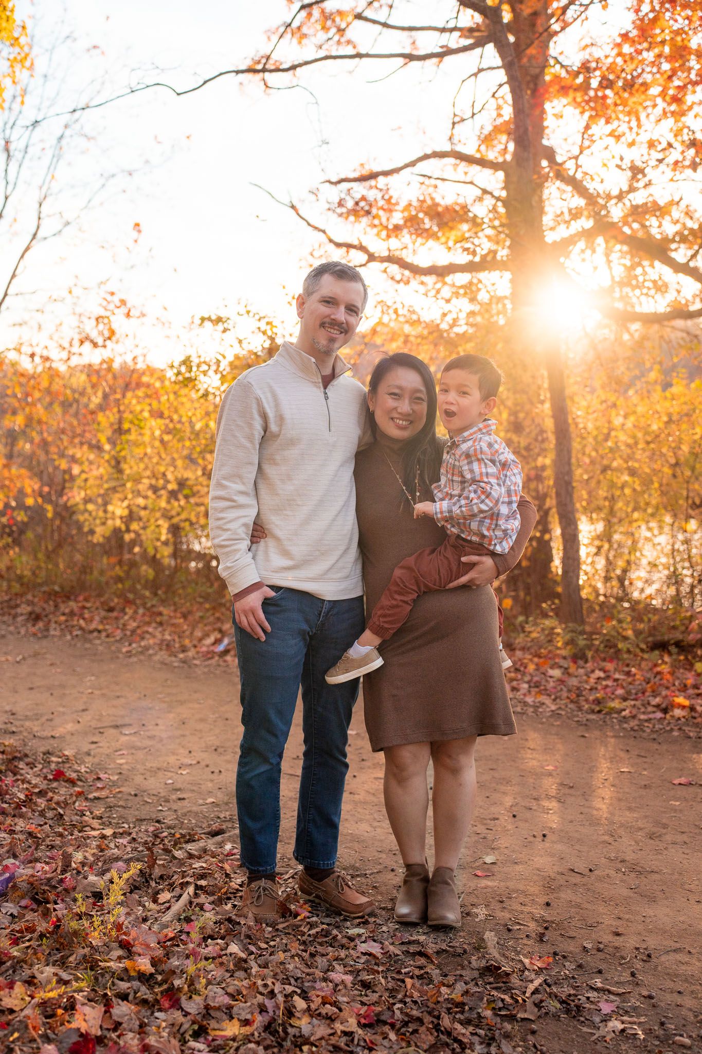 A family poses together on an autumn trail with golden foliage and sunlight streaming through the trees.