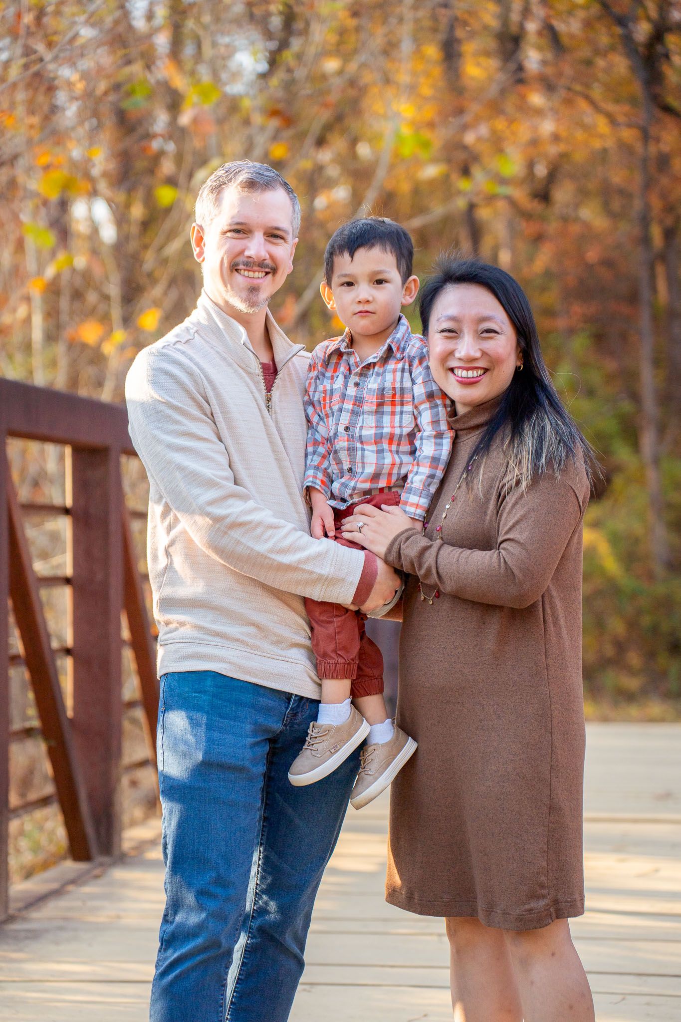 A family shares joyful moments together on a wooden bridge surrounded by autumn foliage in the background.