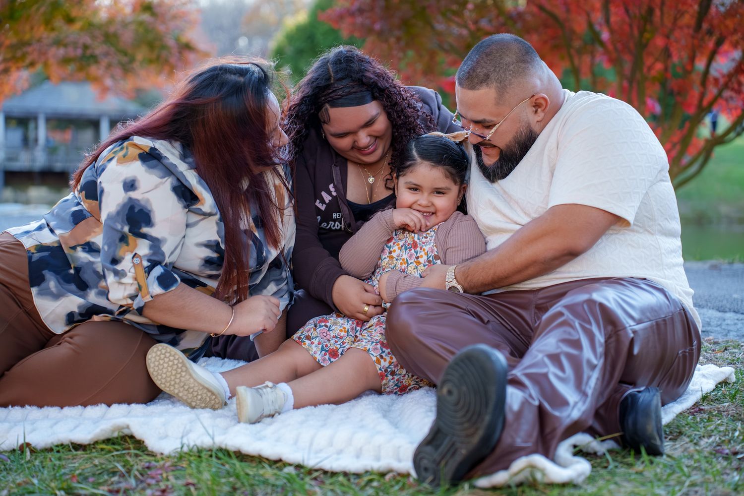Family enjoying outdoor picnic together on blanket surrounded by vibrant autumn foliage in park setting.