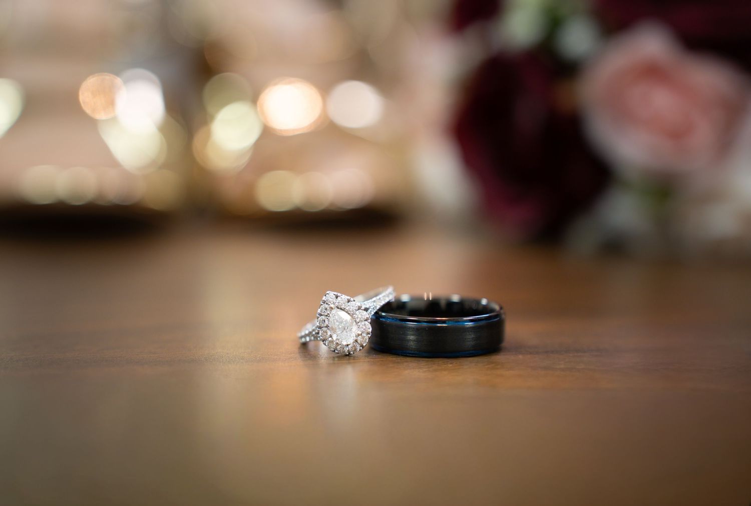 Diamond engagement ring and wedding band displayed with blurred floral decor.