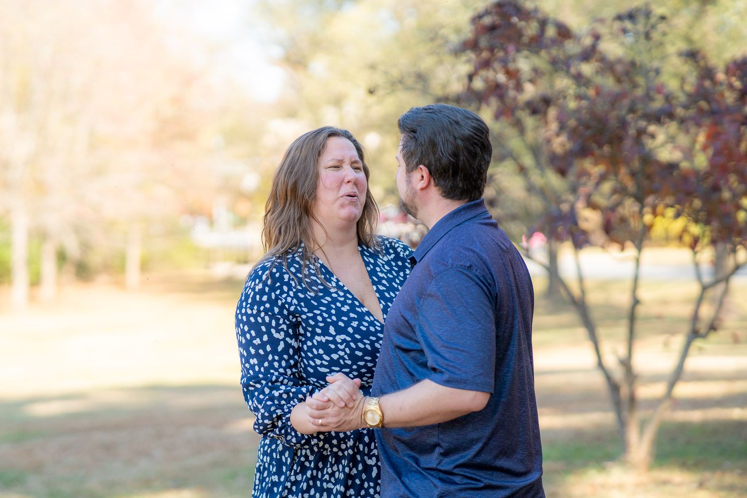 Couple in blue outfits share tender moments during an outdoor autumn photoshoot in a sunlit park setting.