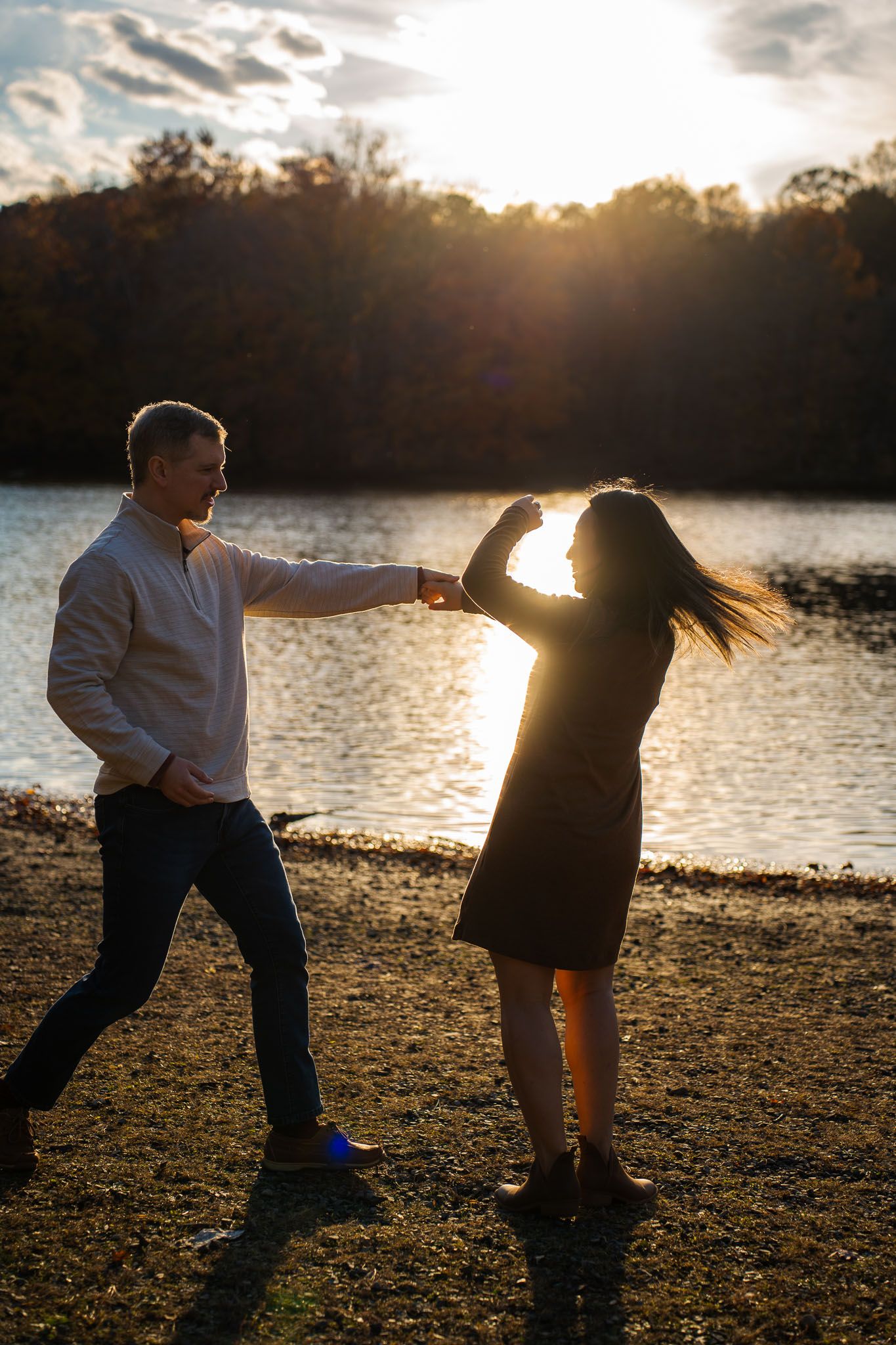 Playful dance moves silhouetted against sunset lake backdrop during outdoor photo session.