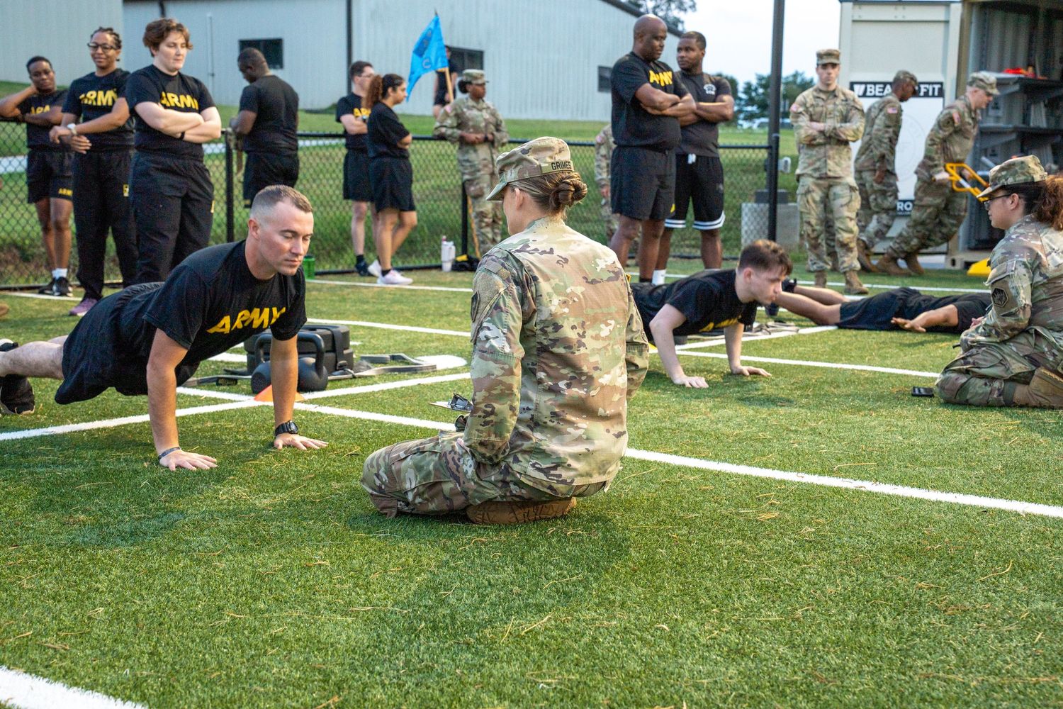 Military personnel perform physical training exercises on a grassy field during an outdoor training session.