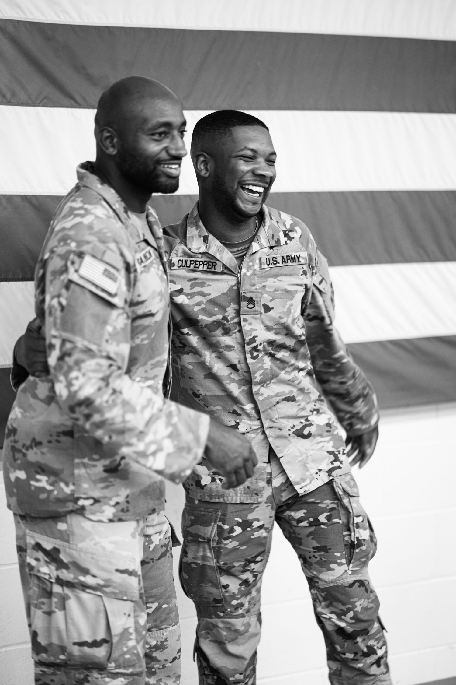 Service members in camouflage uniforms share a lighthearted moment during a military ceremony.