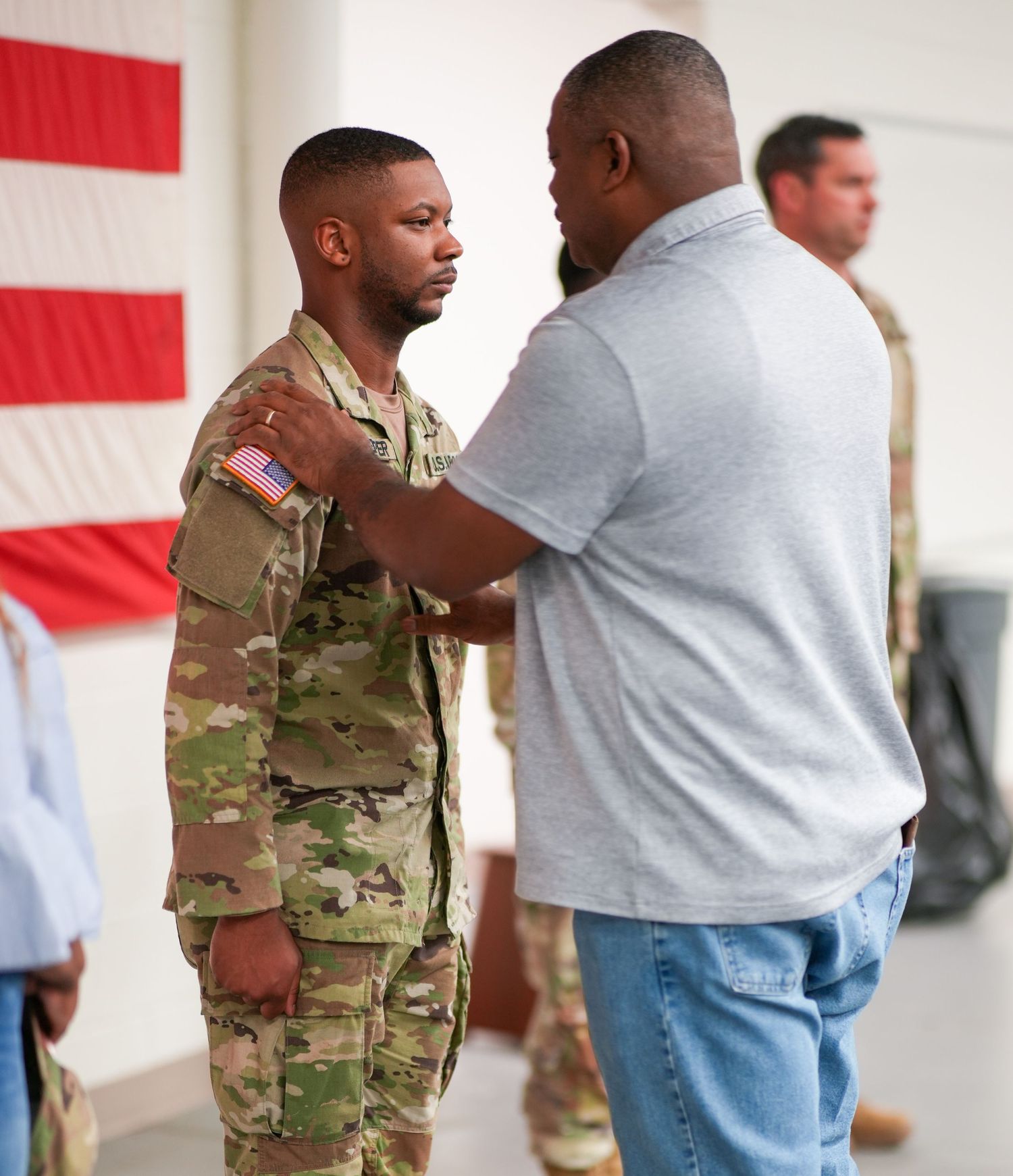 Military promotion ceremony taking place in front of an American flag backdrop.