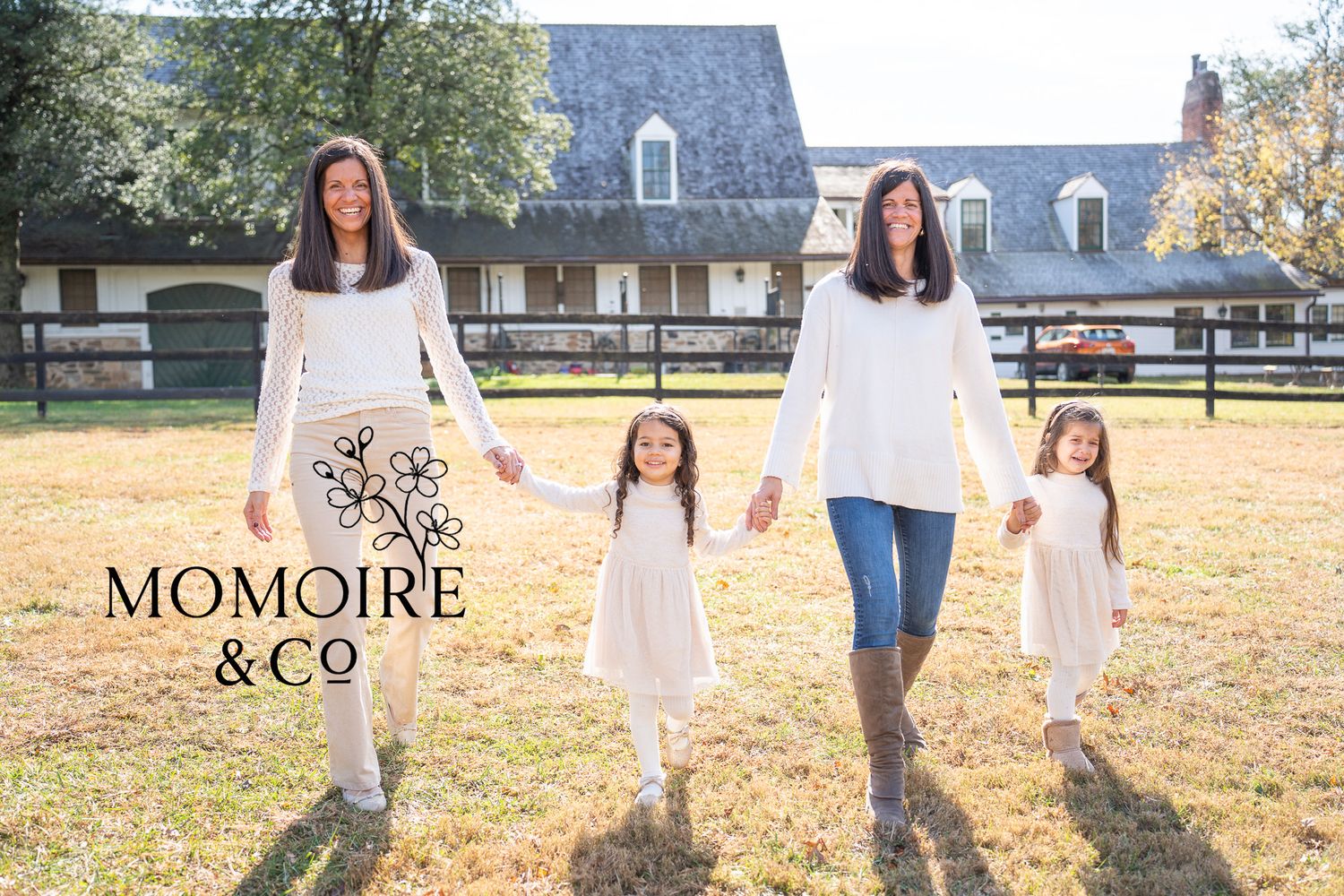 A family wearing coordinated white and blue outfits walks together in a sunlit autumn field during a photo session.