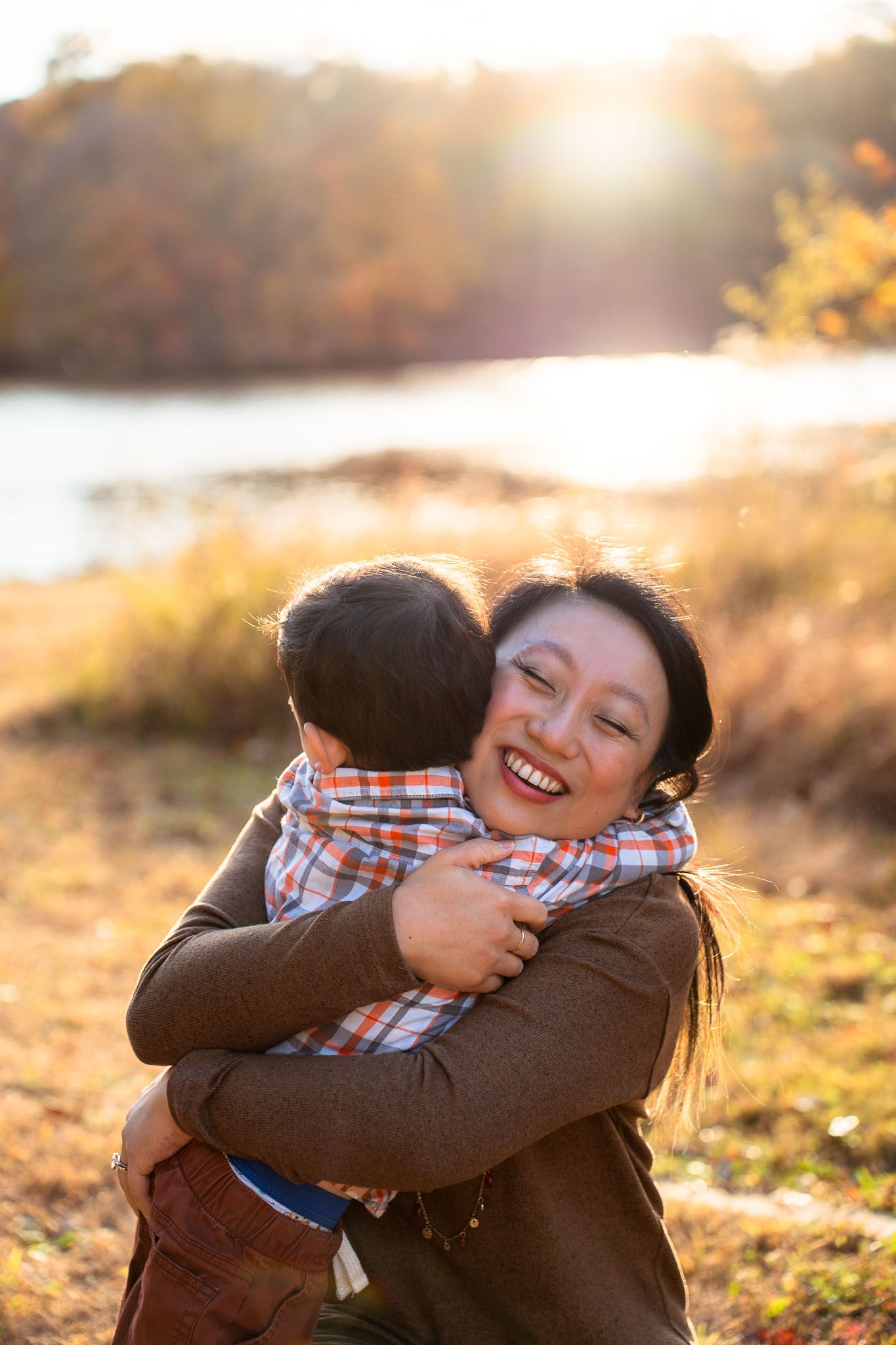 A warm sunset embrace between parent and child in an autumn field with golden light filtering through the background.