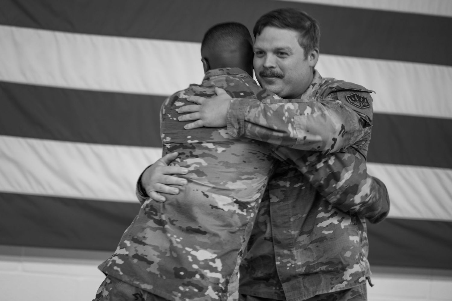 A sequence of black and white photos capturing an emotional military homecoming moment against a dark background.