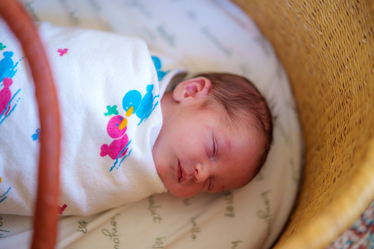 A sleeping baby rests peacefully in a white outfit with colorful floral designs.