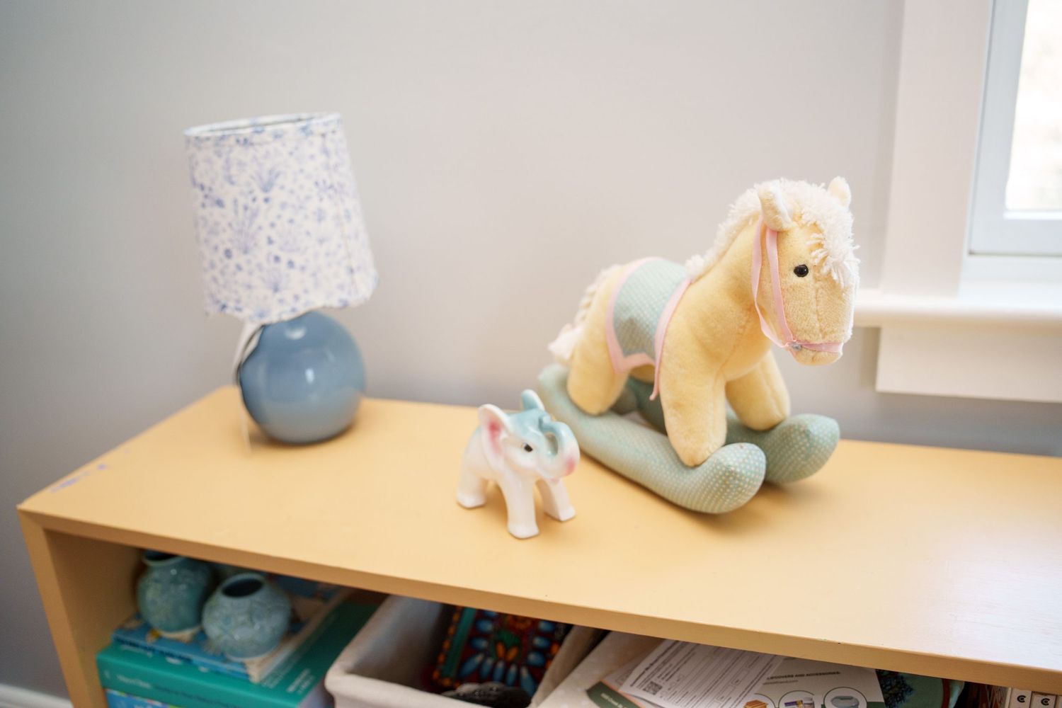 A light wooden desk setup with decorative plush toys and vases in a minimalist room with natural lighting.