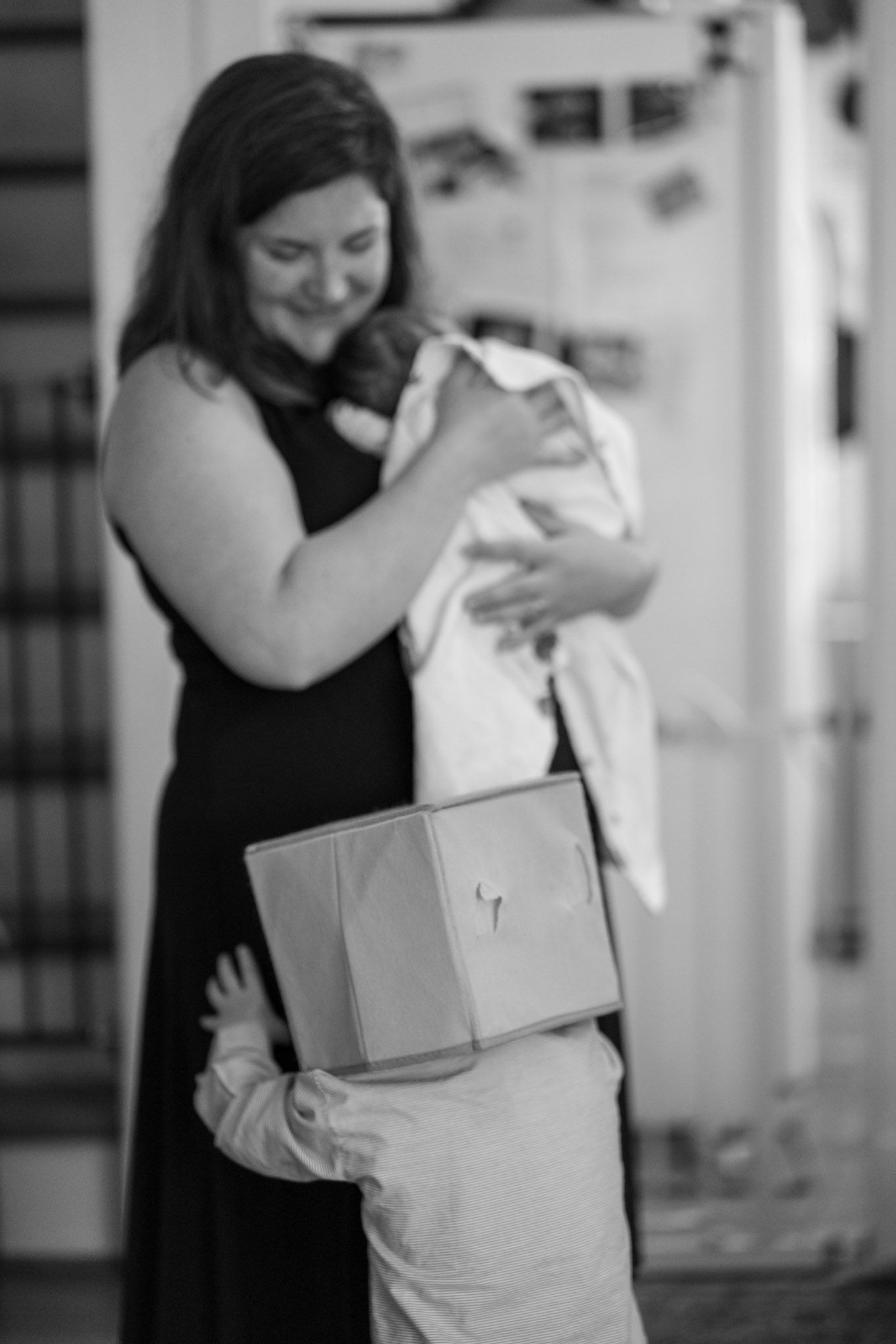 A woman in black holds and embraces a white wrapped bundle with care and tenderness. Silver Spring Lifestyle Newborn Photographer