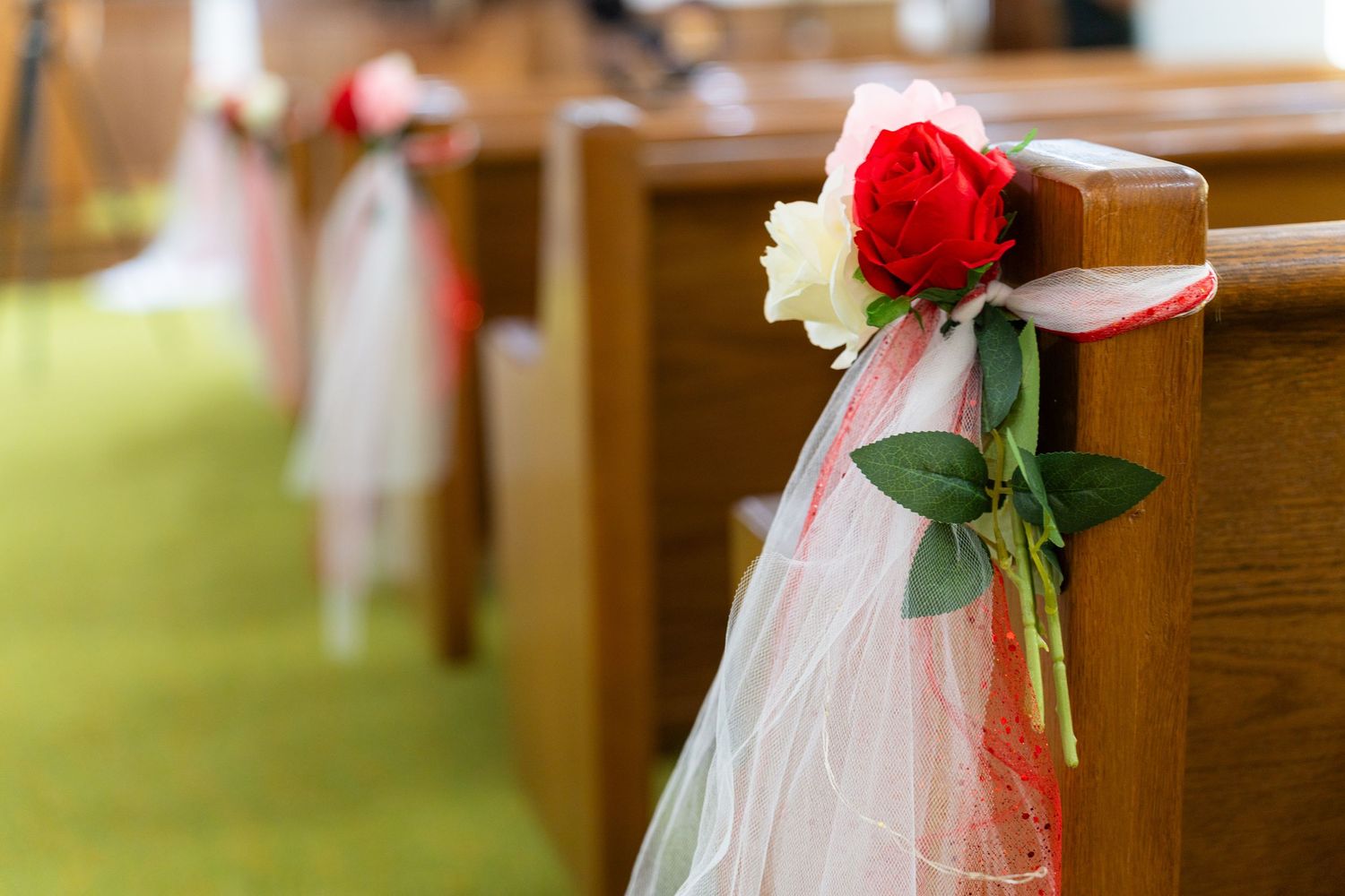 Red and white tulle bows with roses decorate wooden church pews for a wedding ceremony.