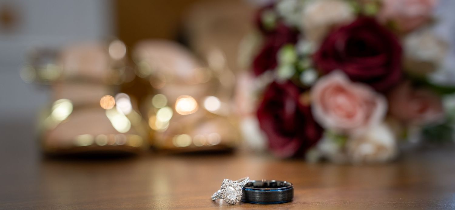 Close-up of wedding rings with soft bokeh lights and floral decorations in background.