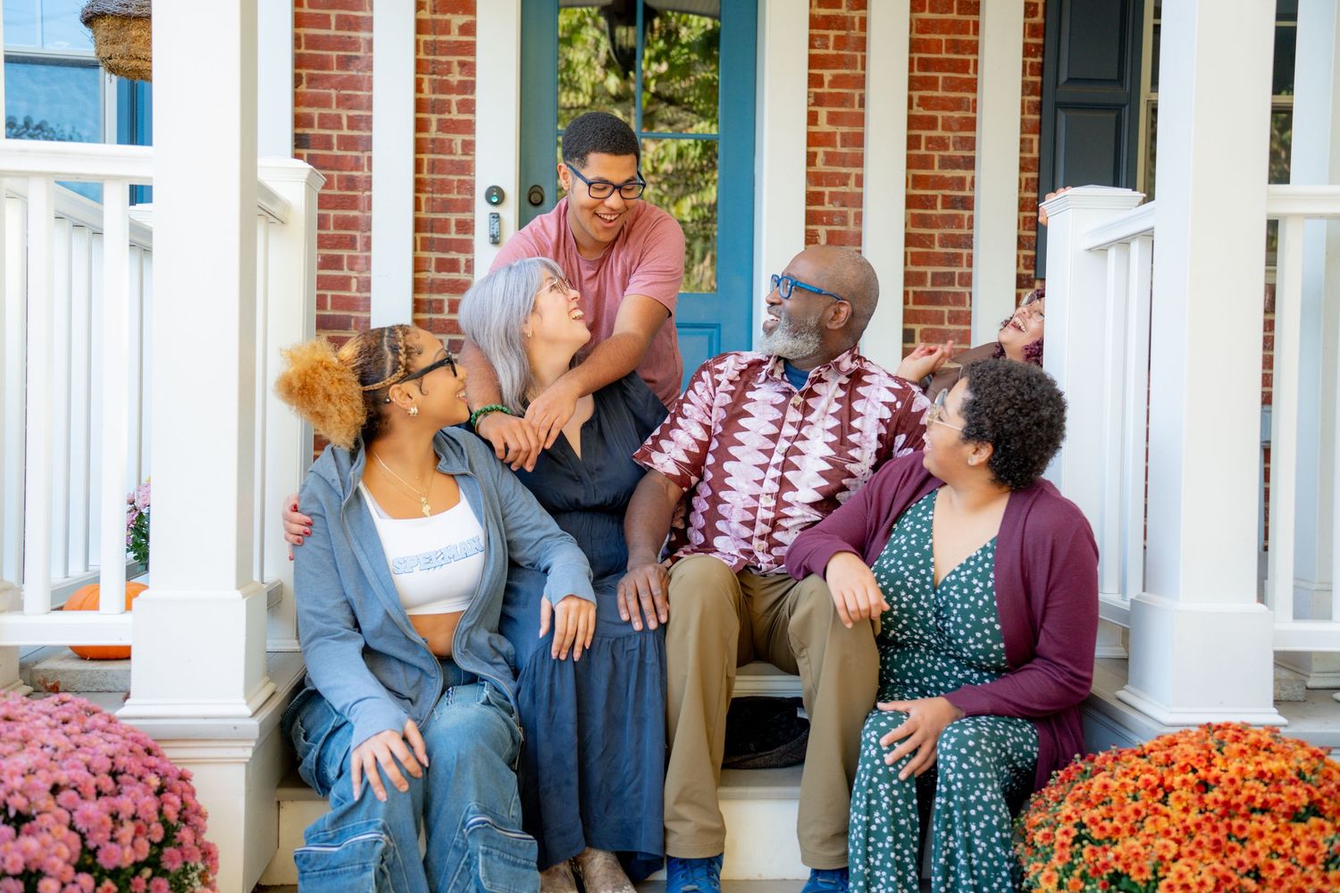 Lovely family sitting and laughing on a front porch of their brick home with white columns.