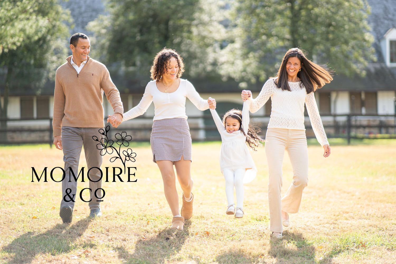 Family members hold hands while walking together through a sunlit field on a warm autumn day.