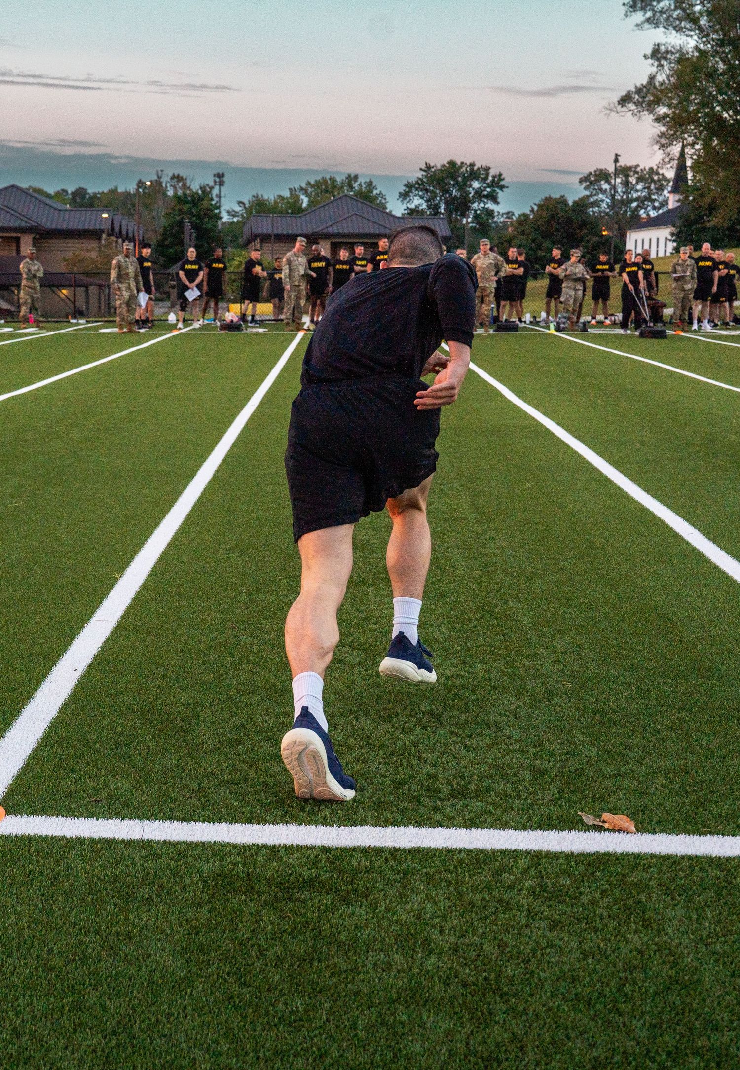 Person walking on a freshly lined soccer field at dusk with residential buildings in the background.