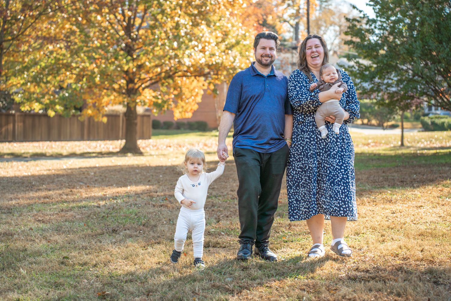 Family enjoying autumn scenery with golden leaves and sunlight in outdoor park setting.