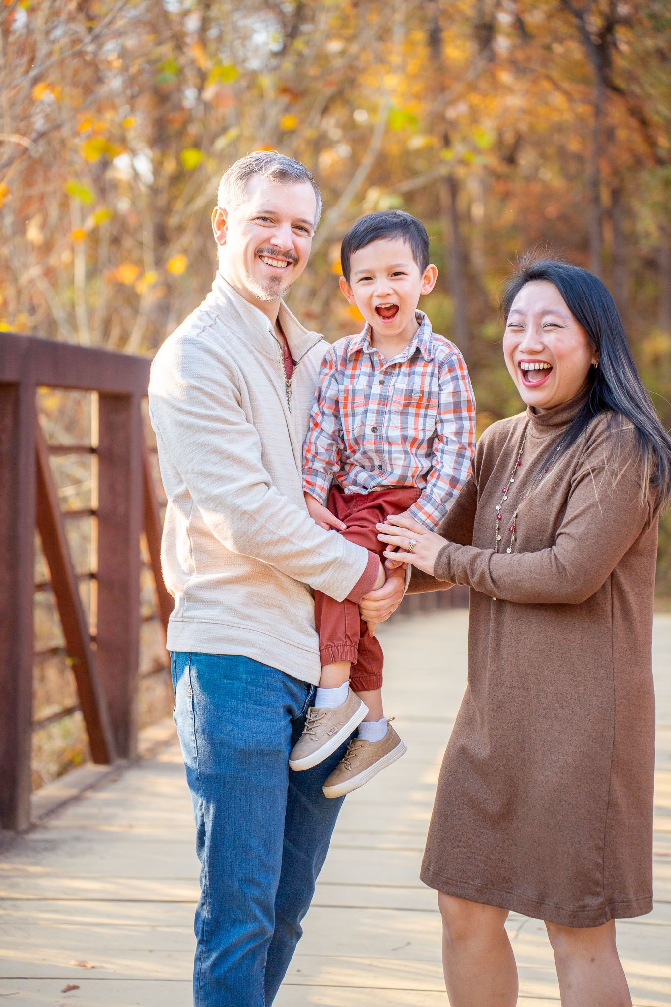 A joyful family shares laughter together on a wooden bridge surrounded by autumn foliage.